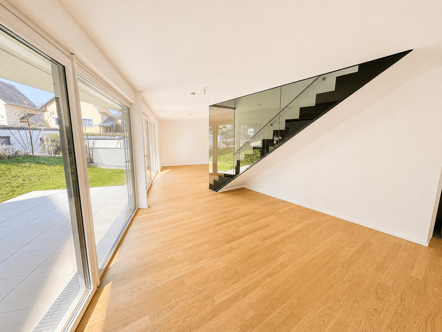 Geräumiger Wohnbereich mit Eichenparkett, moderner Treppe und großen Fenstern zum Außenbereich.