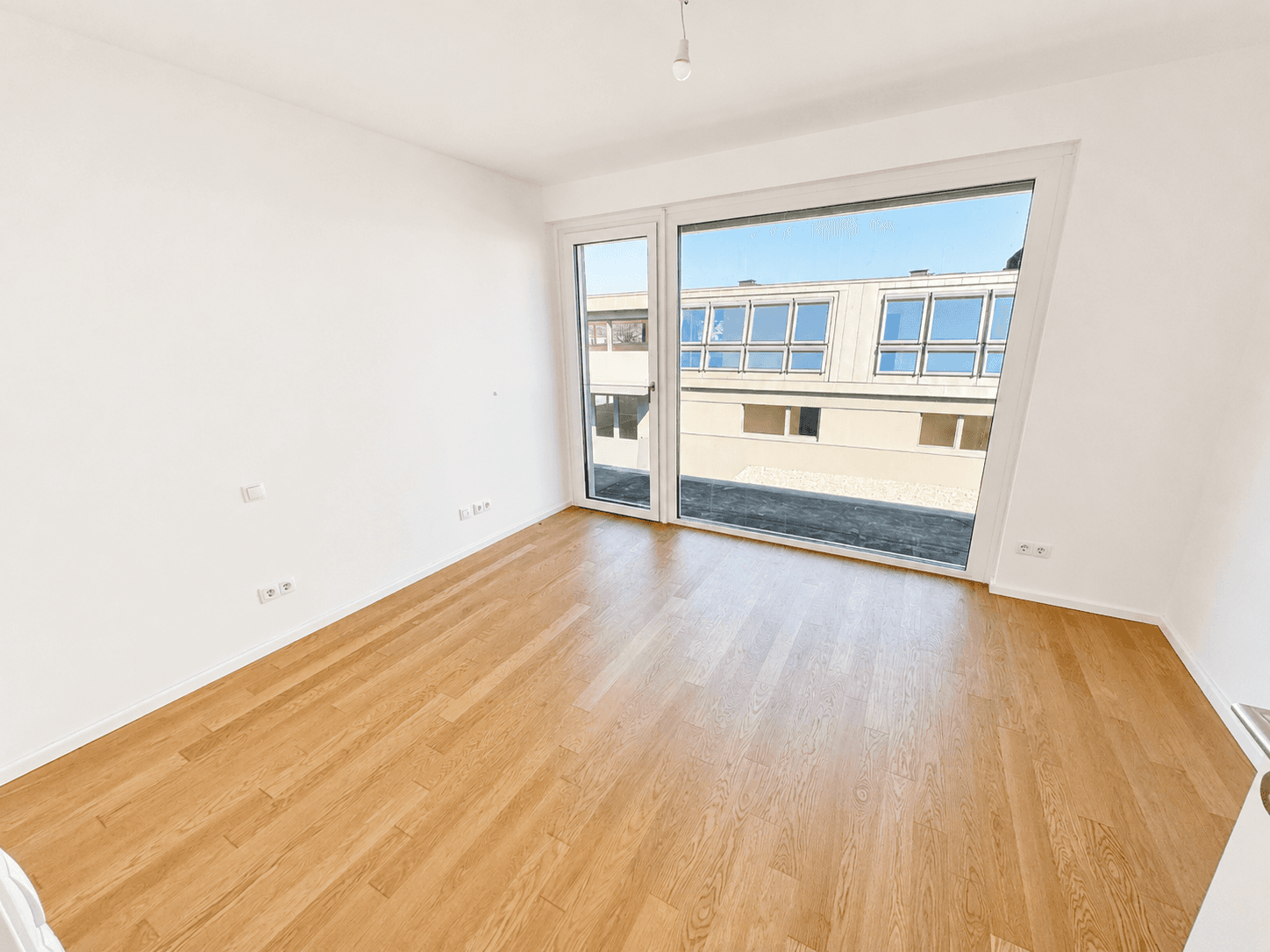 Helles Schlafzimmer mit Eichenparkett und großem Fenster mit Blick auf gegenüberliegende Gebäude.