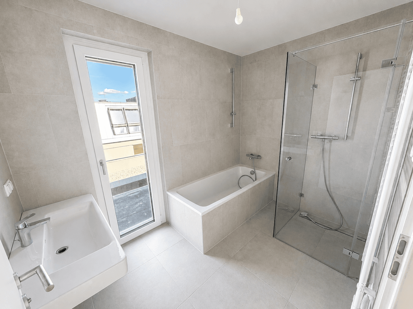 Helles Badezimmer mit Badewanne, Dusche, Einzelwaschbecken und Zugang zu einem Außenbereich.