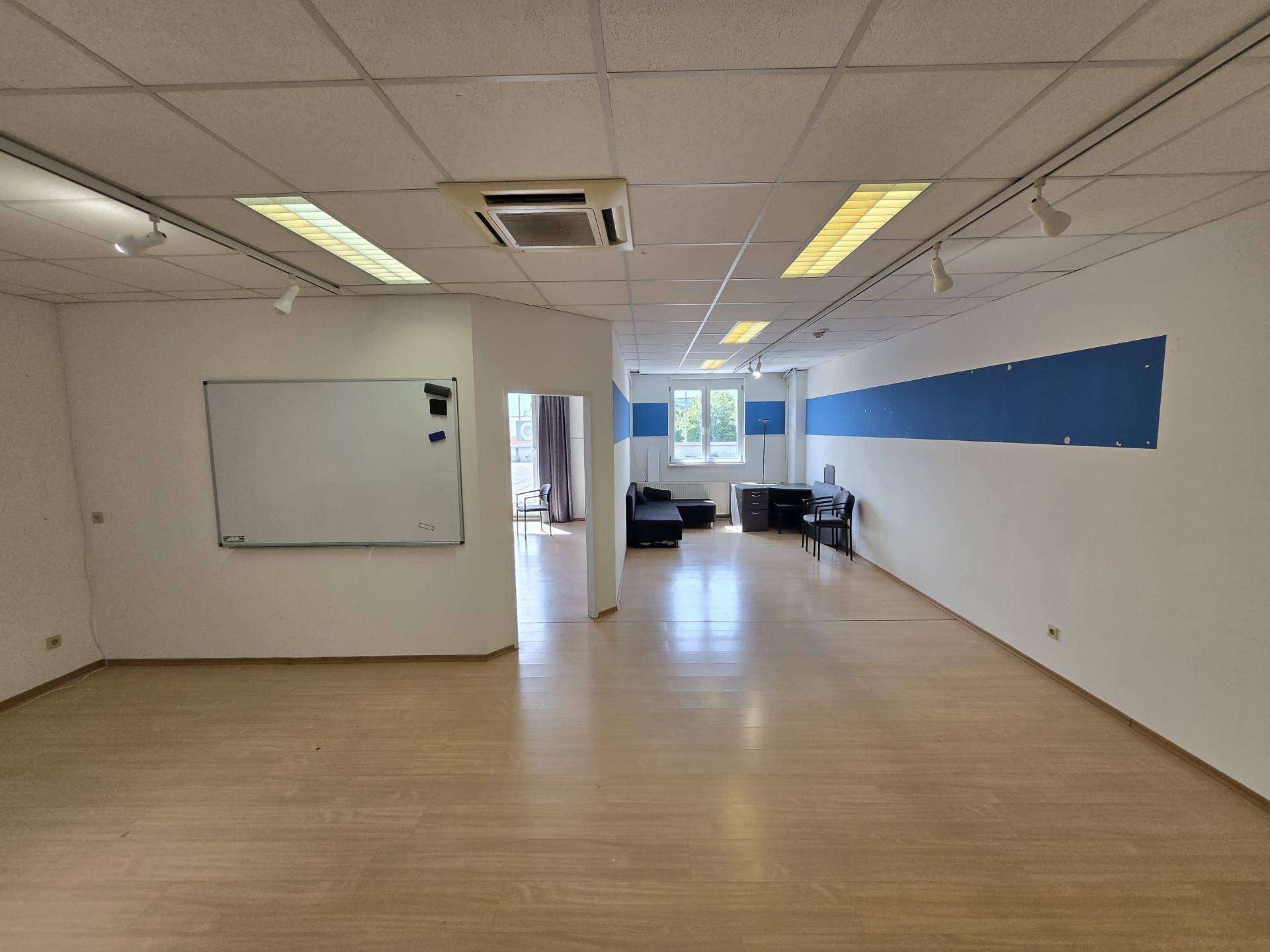 Großer, offener Bürobereich mit Laminatboden, Whiteboard und Blick in einen weiteren Raum.
