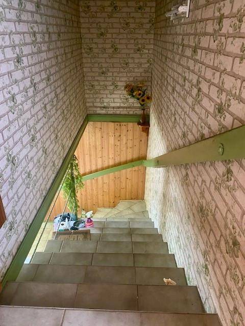 Treppenhaus mit gefliesten Stufen und Tapete im Ziegelmuster, das in den unteren Bereich führt.