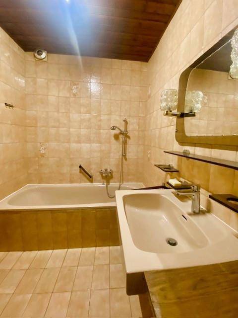 Badezimmer mit beigefarbenen Fliesen, Badewanne, Waschbecken und einer Holzdecke im traditionellen Stil.