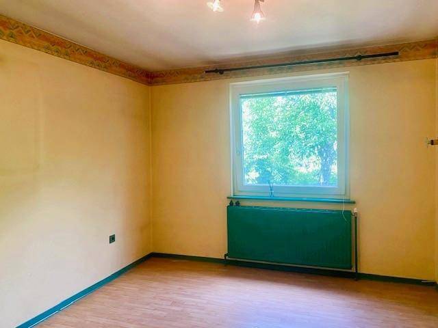 Helles Zimmer mit gelben Wänden, Holzboden und einem grünen Heizkörper unter dem Fenster.