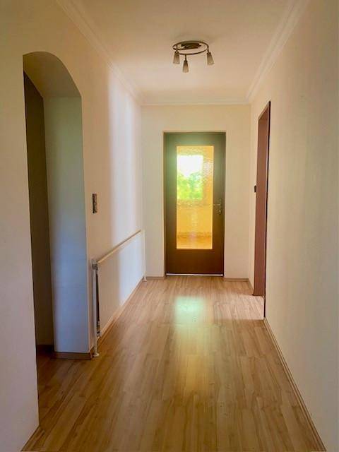 Heller Flur mit Holzboden und einer Tür mit Glaseinsatz, die Tageslicht hereinlässt.
