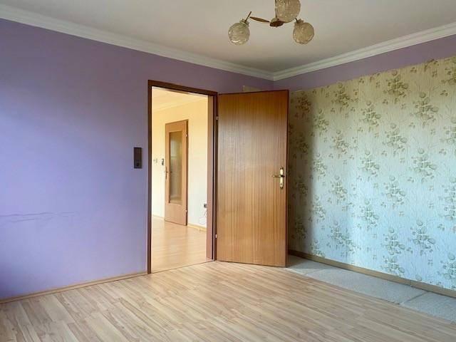 Zimmer mit lila Wänden und floraler Tapete, ausgestattet mit einem Holzboden und einer Holztür.