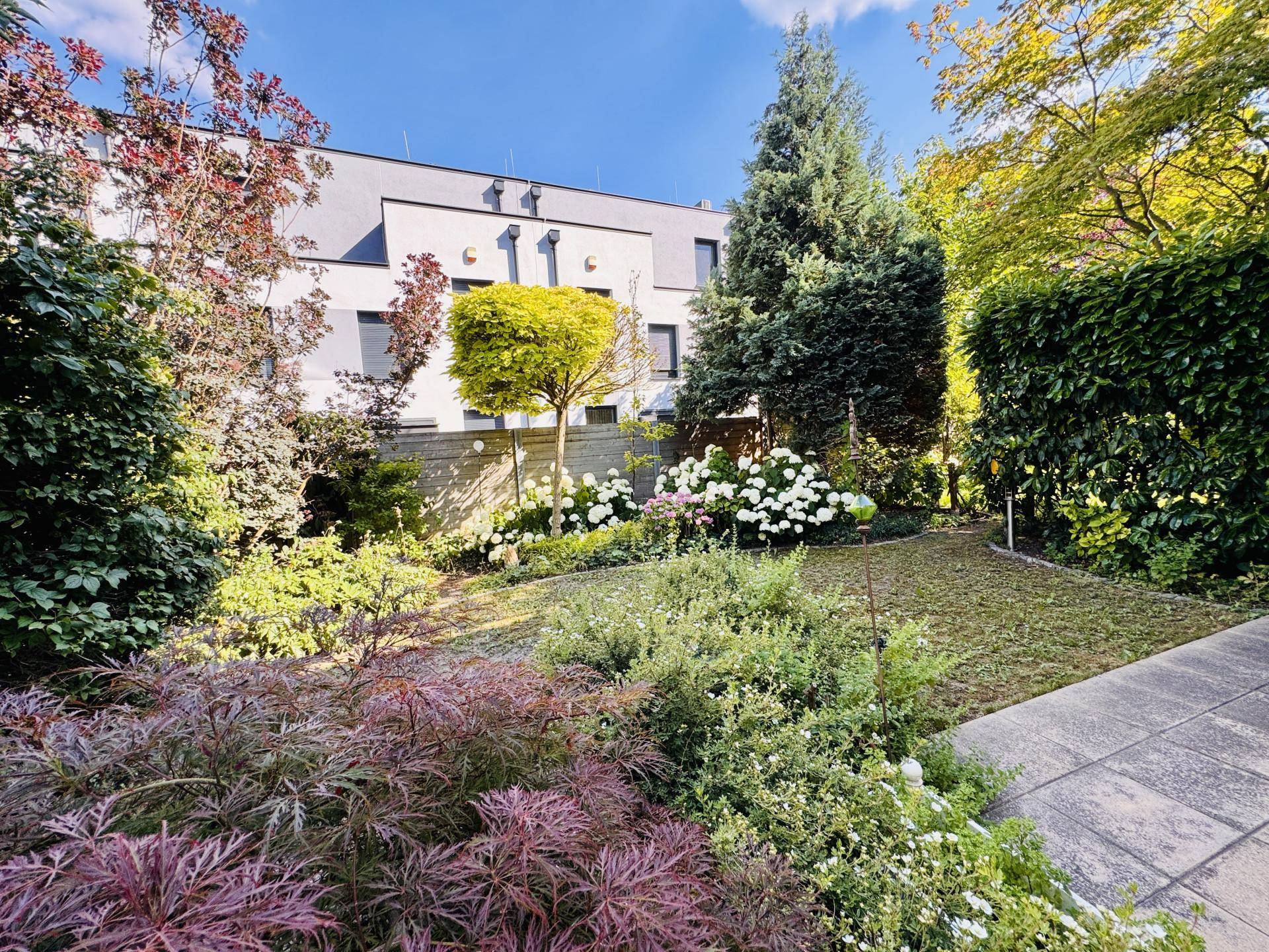 Großer, gepflegter Garten mit vielfältiger Bepflanzung, Rasenfläche und hohen Bäumen.