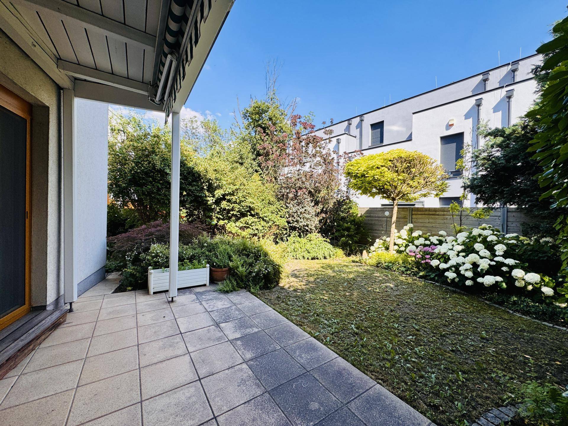 Sonniger Terrassenbereich mit Fliesenboden und direktem Zugang zum grünen Garten.