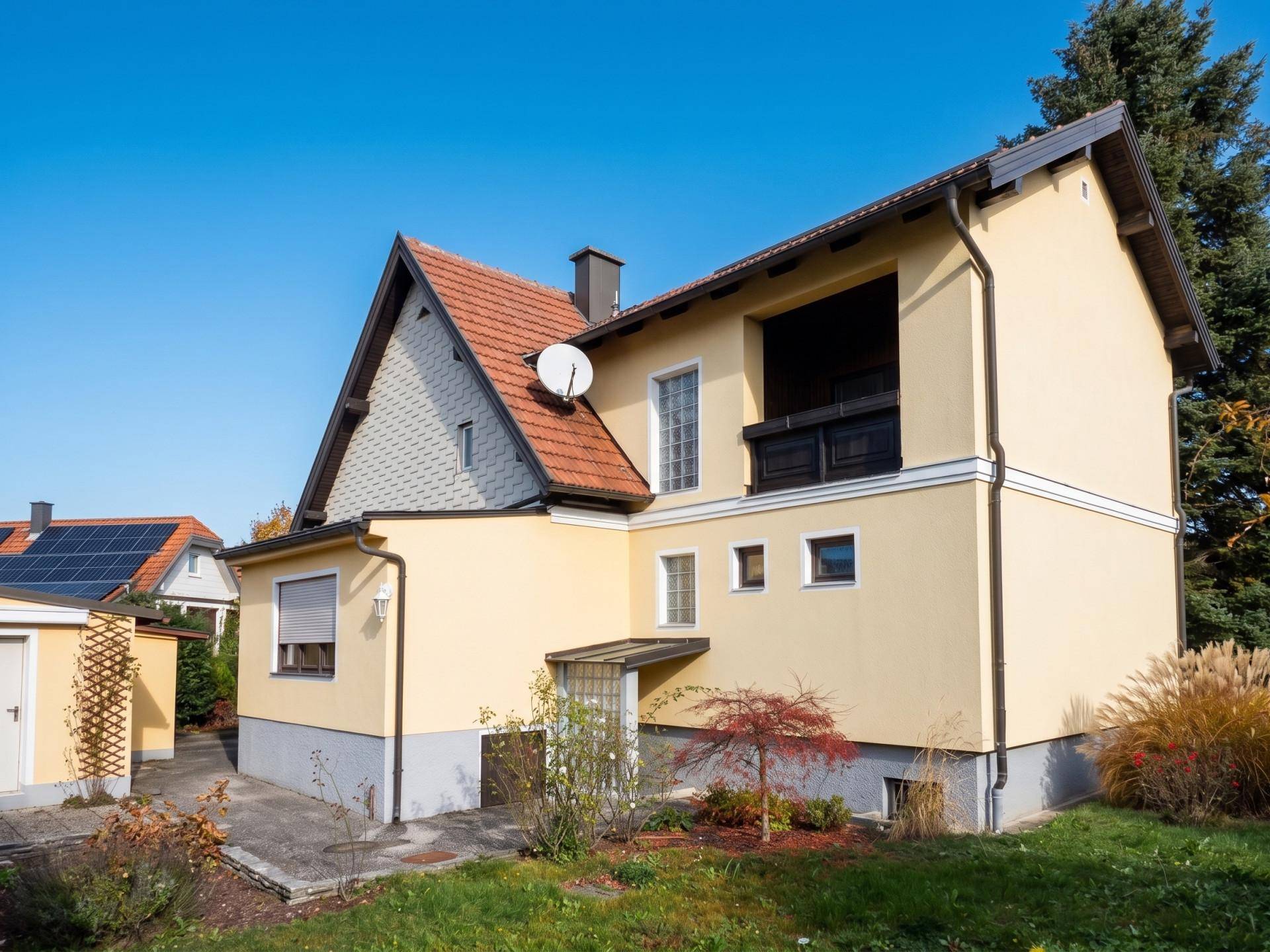 Rückansicht des gelben Hauses mit Loggia, Satteldach und Solaranlage auf Nebengebäude.