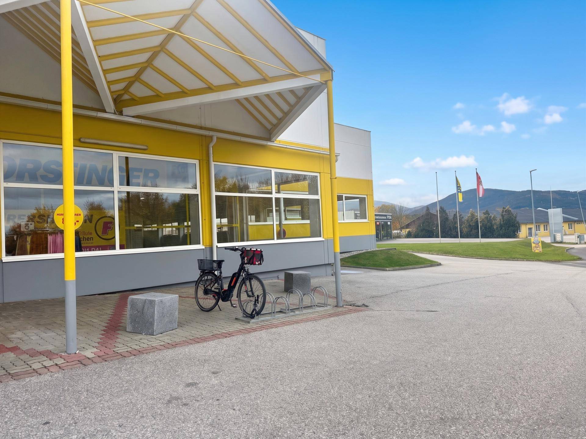 Eingangsbereich eines Geschäftsgebäudes mit Überdachung, Fahrradstellplatz und Blick auf die Berge.