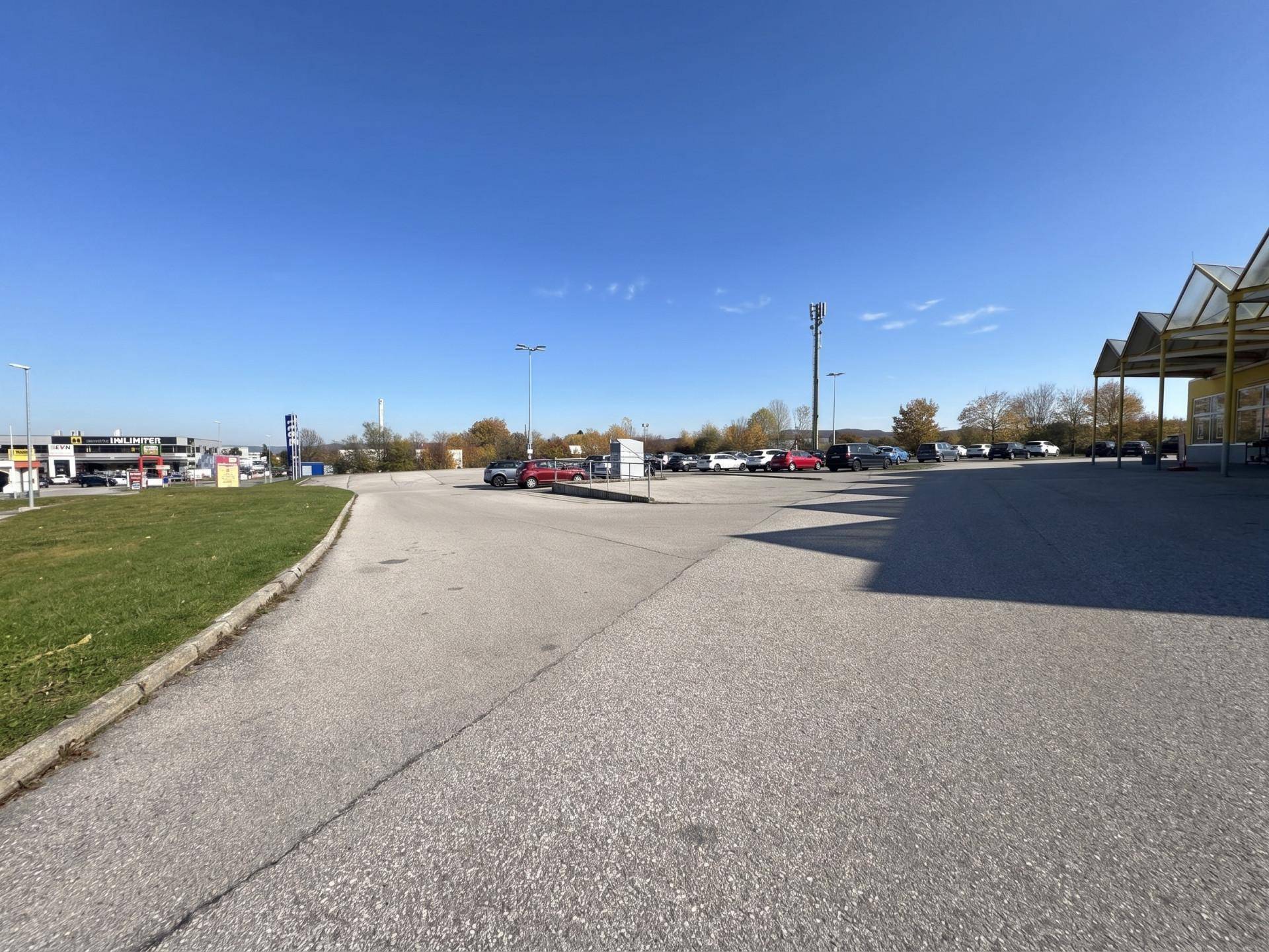 Weitläufiger Parkplatz vor einem Geschäftsgebäude unter klarem blauem Himmel.