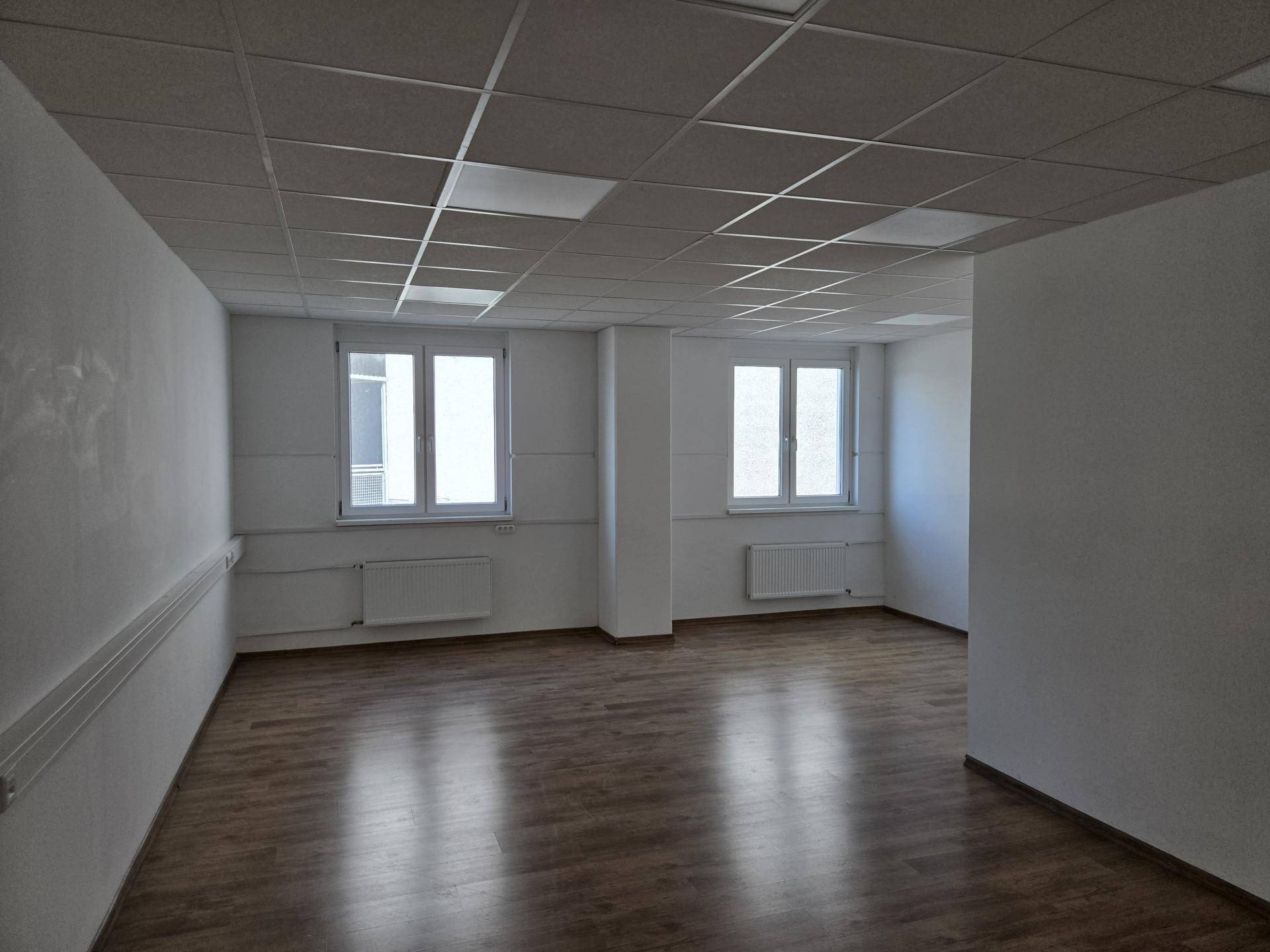 Heller Büroraum mit Laminatboden und zwei Fenstern, die für eine angenehme Arbeitsatmosphäre sorgen.