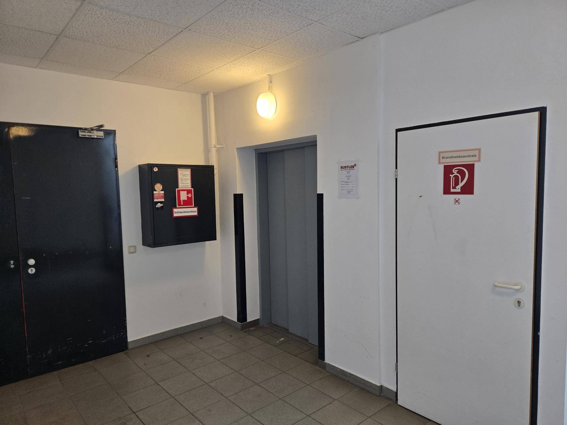 Flur mit Aufzug, Brandschutzvorrichtungen und Zugang zu verschiedenen Räumlichkeiten.