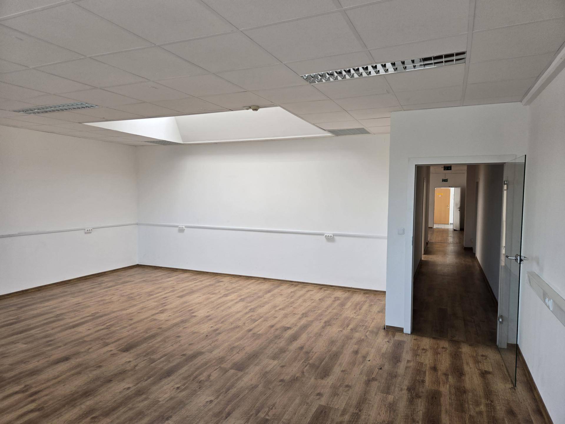 Heller Büroraum mit Laminatboden, abgehängter Decke und einer Glastür zum Flur.