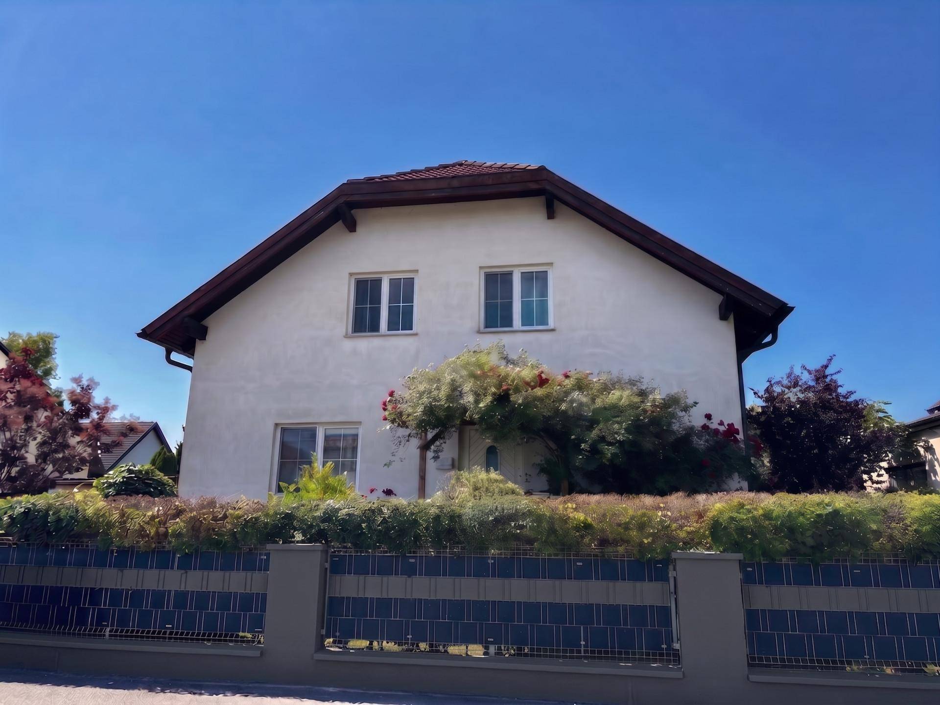 Ansicht der Hausfassade von der Straße mit gepflegter Hecke und Fenstern.