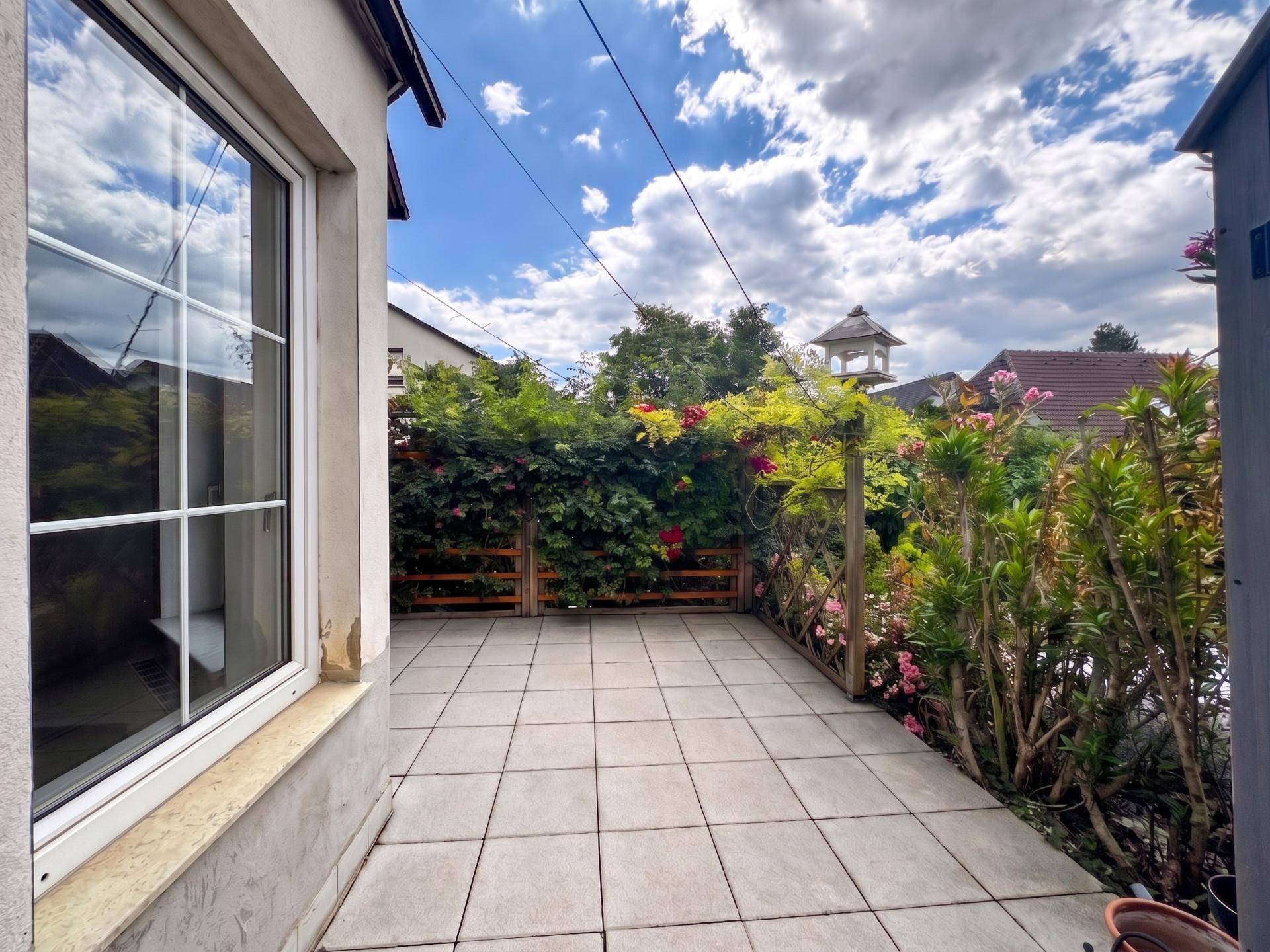 Gemütliche gepflasterte Terrasse mit viel Grün und Holzzaun, ideal für Entspannung.