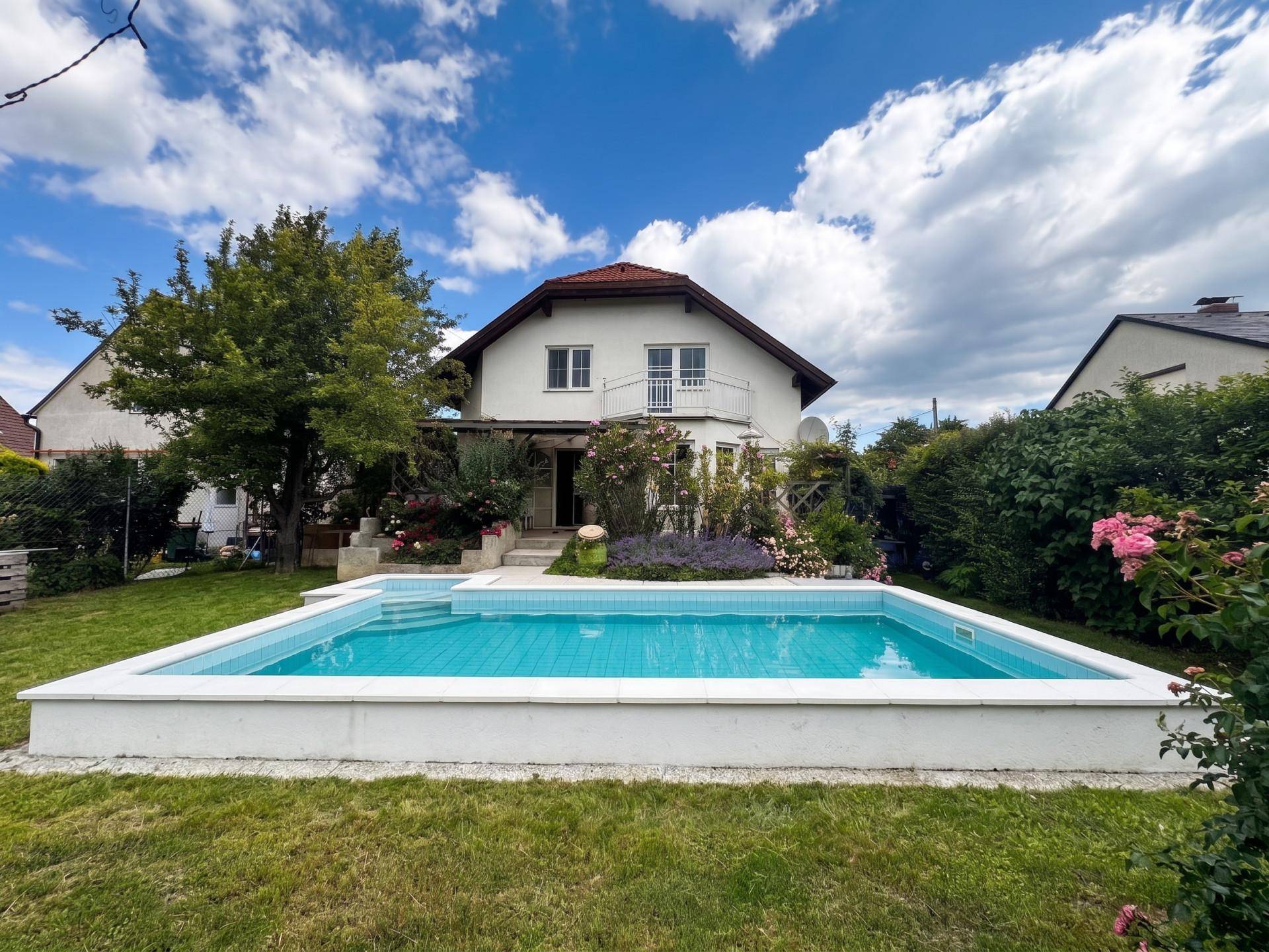 Gepflegter Gartenbereich mit rechteckigem Pool und blühenden Pflanzen vor dem Haus.