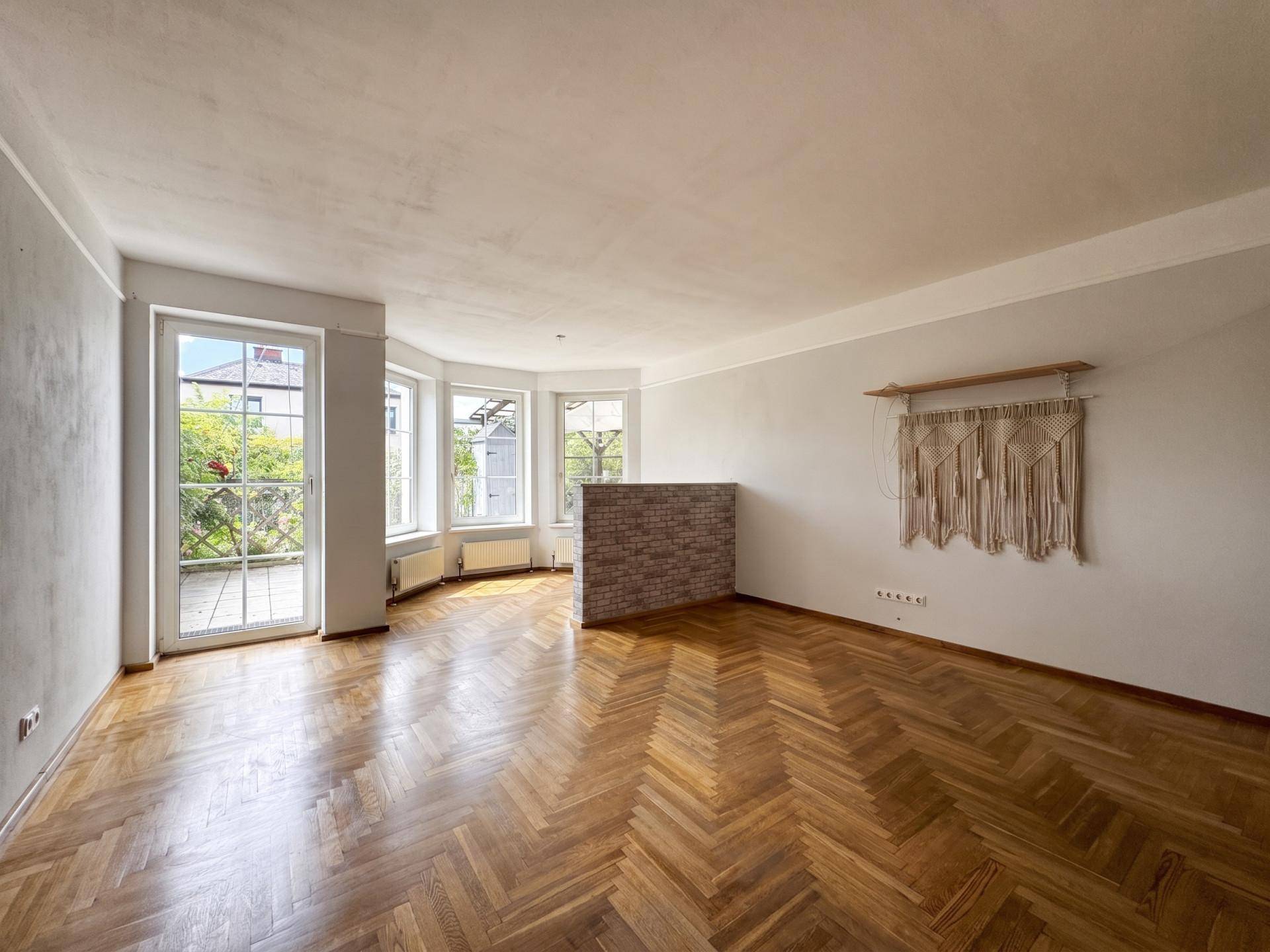 Geräumiges Wohnzimmer mit Fischgrätparkett, großen Fenstern und Zugang zur Terrasse.