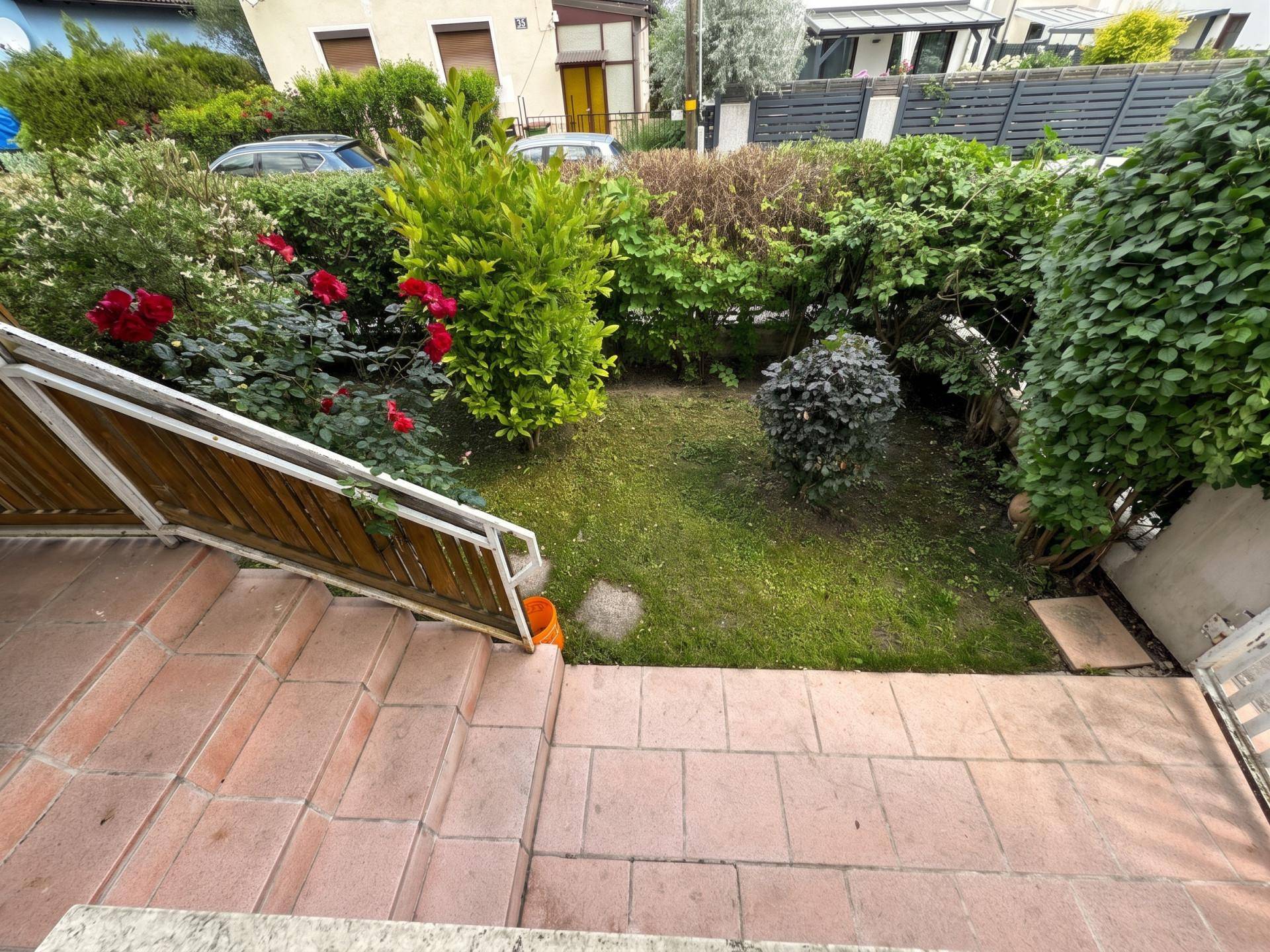 Kleiner Gartenbereich mit Stufen und blühenden Rosen, umgeben von Hecken.