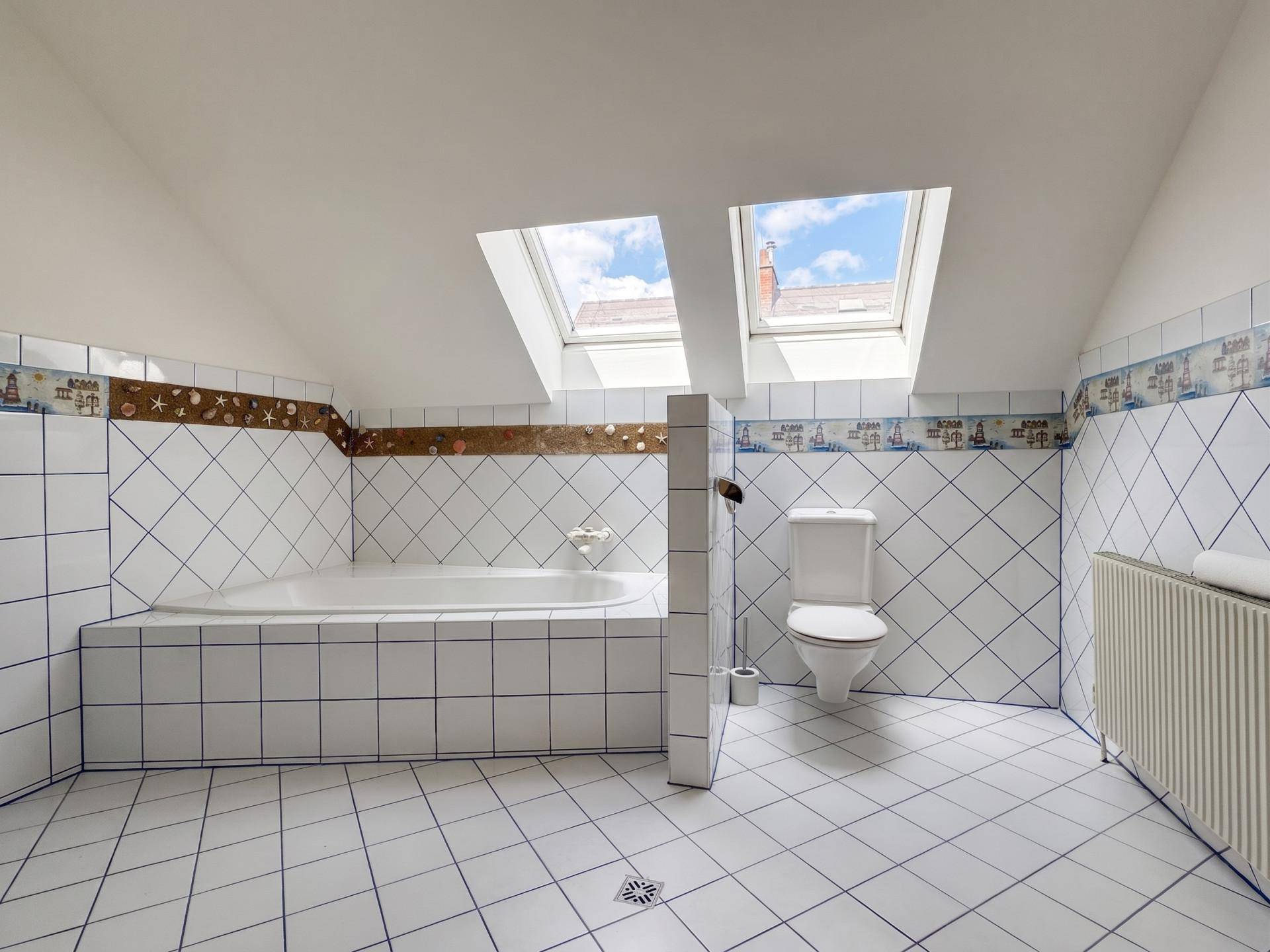 Badezimmer im Dachgeschoss mit Badewanne, WC, Dachfenstern und weißen Fliesen.