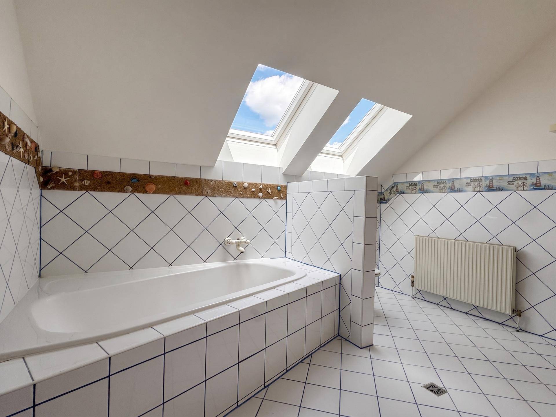 Dachgeschoss-Badezimmer mit eingebauter Badewanne, weißen Fliesen und zwei Dachfenstern.