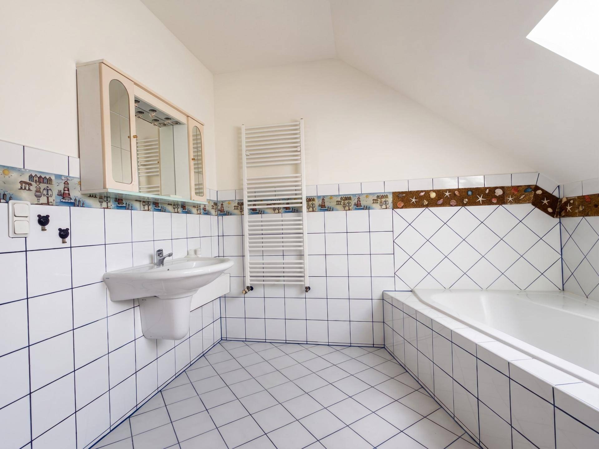 Badezimmer mit Waschbecken, Spiegelschrank, Handtuchheizkörper und weißen Fliesen.