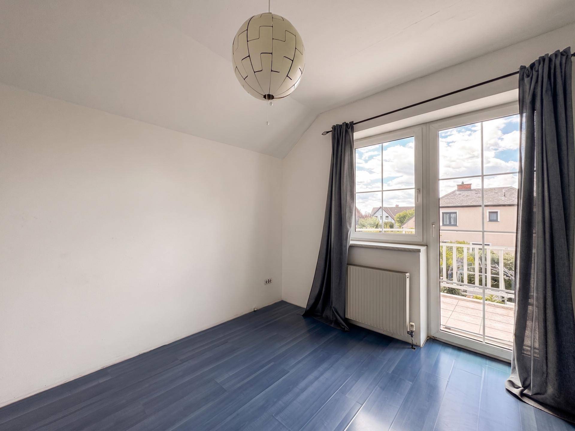 Schlafzimmer mit blauem Holzboden, Fenster und Zugang zu einem Balkon.