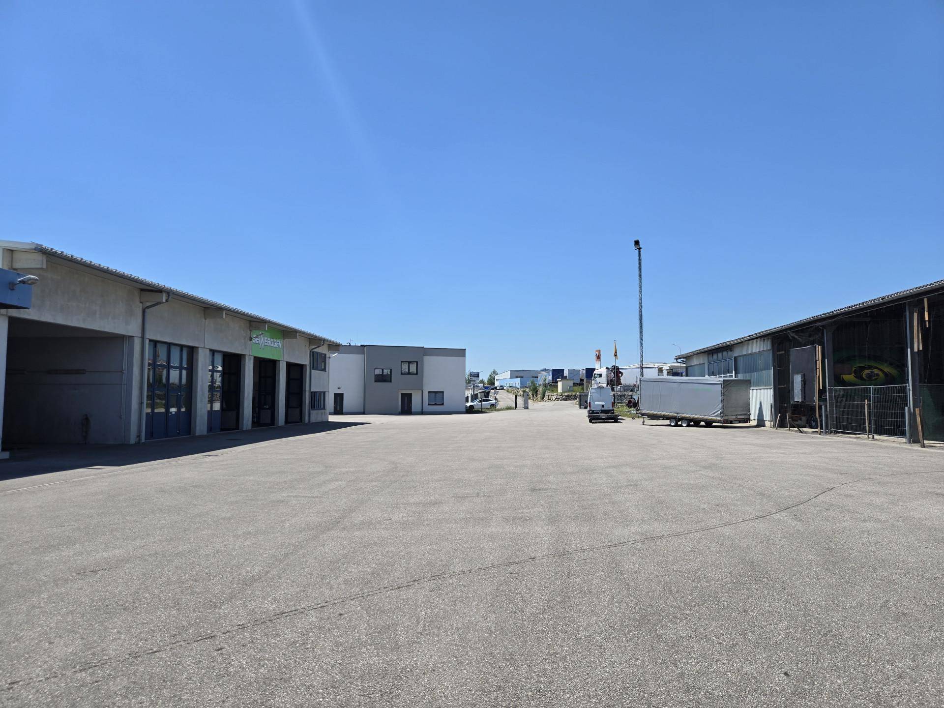 Großer, gepflasterter Vorplatz mit Zufahrt zu verschiedenen Gewerbehallen und Büros bei sonnigem Wetter.