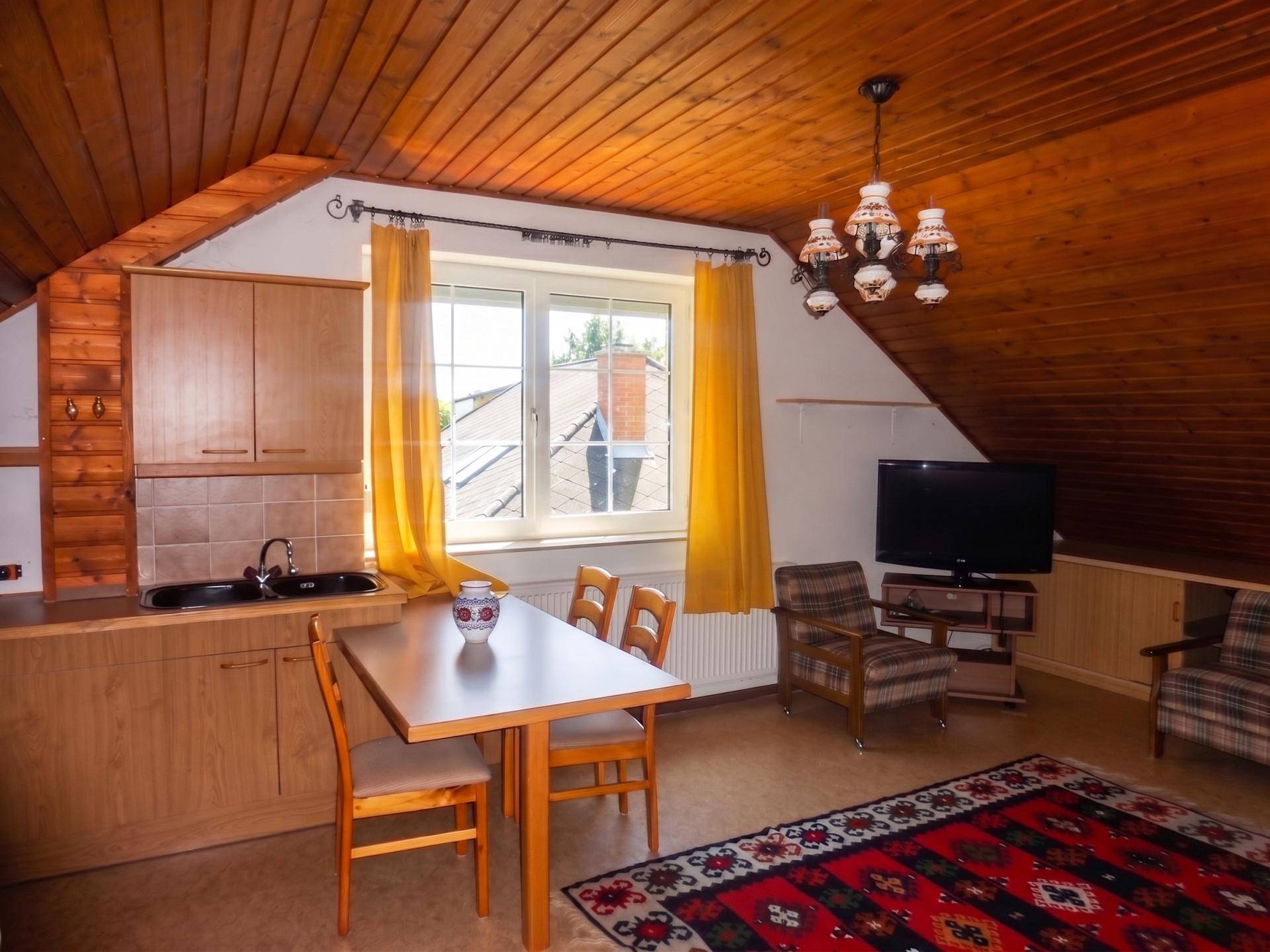 Gemütlicher Wohn-Essbereich im Dachgeschoss mit kleiner Küche und Holzdecke.