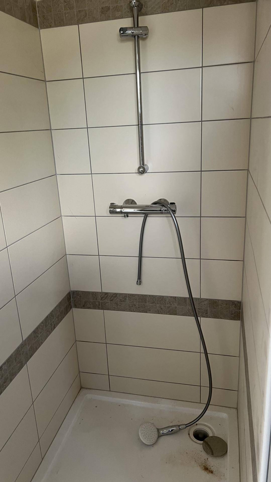 Duschkabine mit hellen Fliesen und einer grauen Dekorleiste.