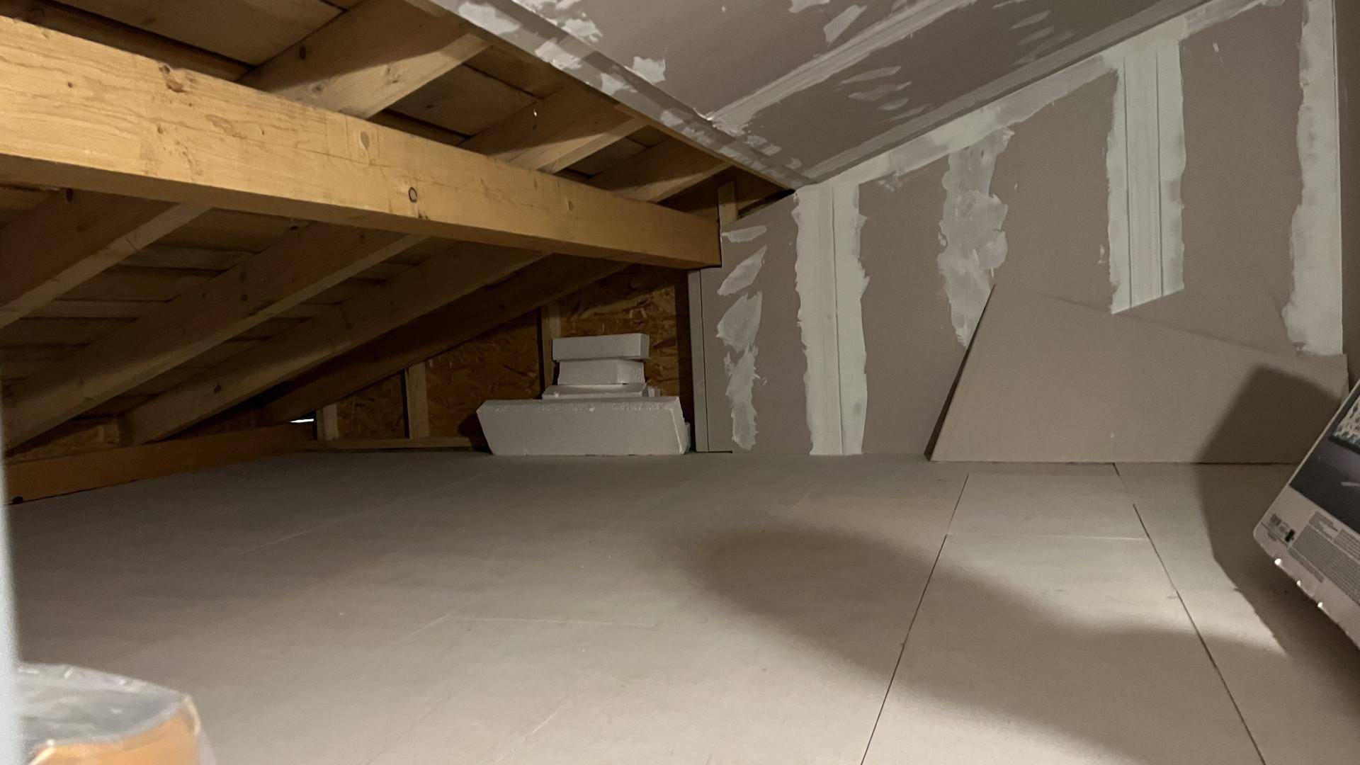 Unausgebauter Dachboden mit sichtbaren Holzbalken und Trockenbauwänden.