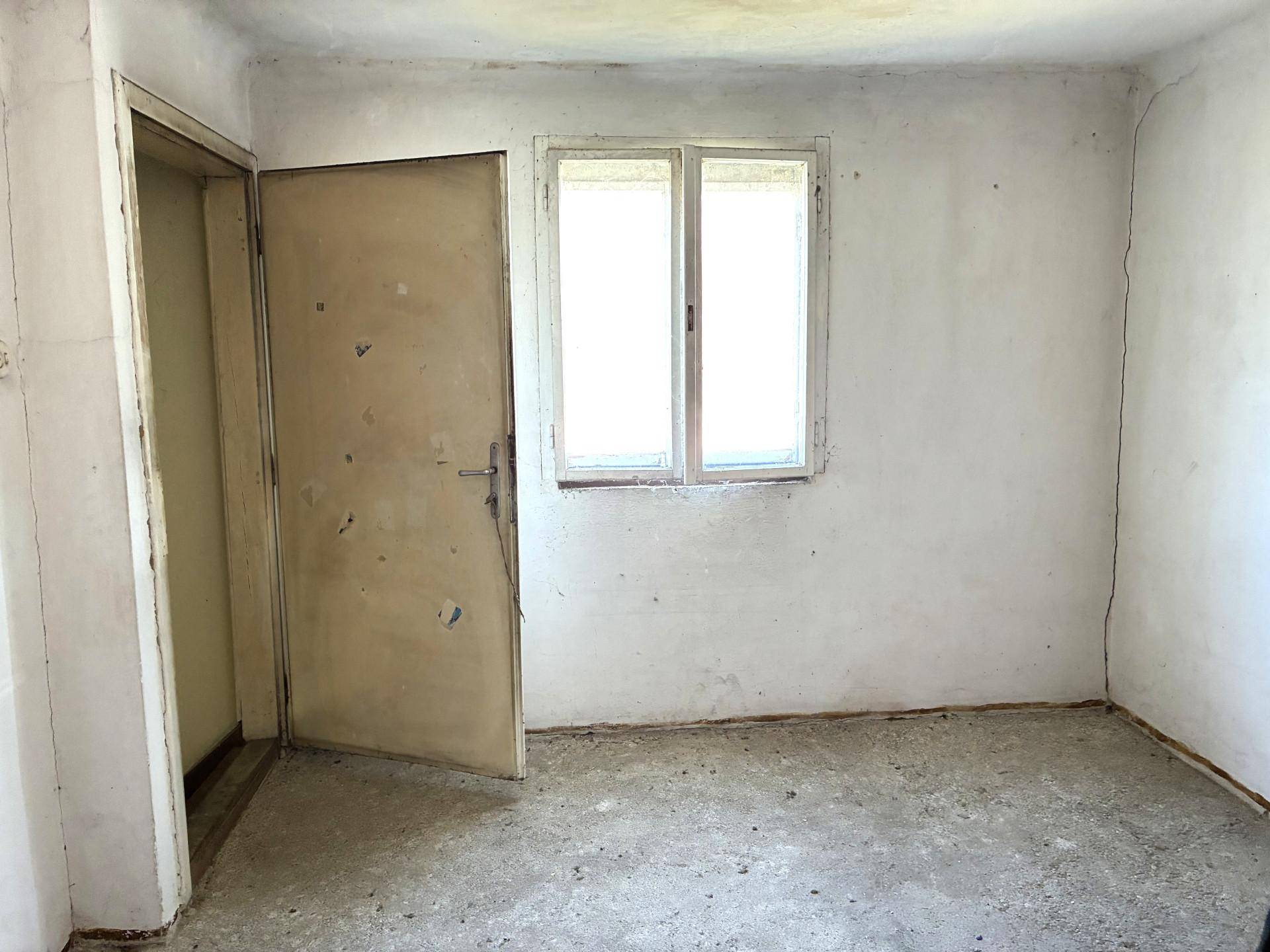 Unmöblierter Raum mit weiß gestrichenen Wänden, einem Fenster und einer einfachen Tür.