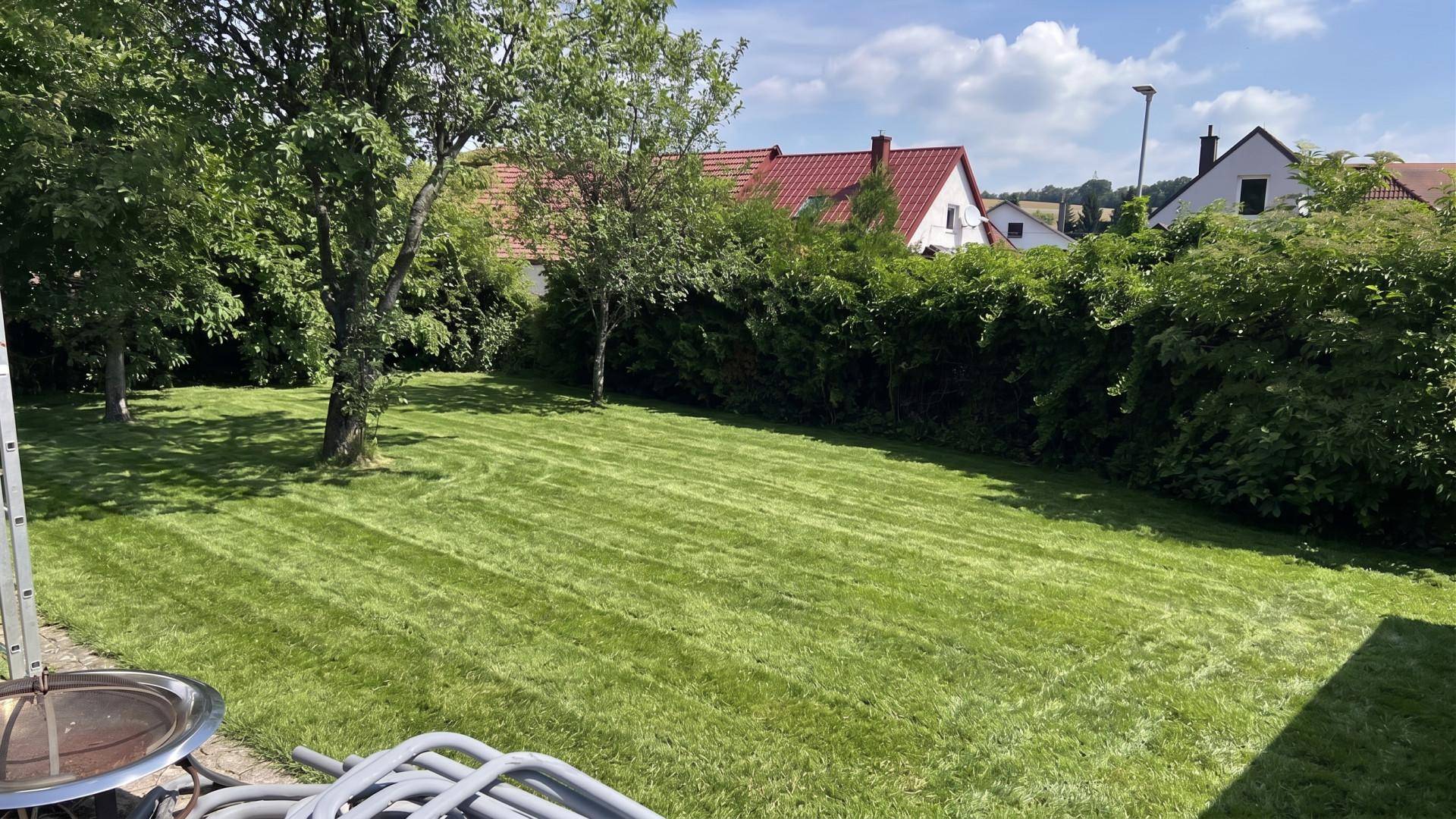 Großer, gepflegter Rasenbereich mit Bäumen und Blick auf benachbarte Häuser.
