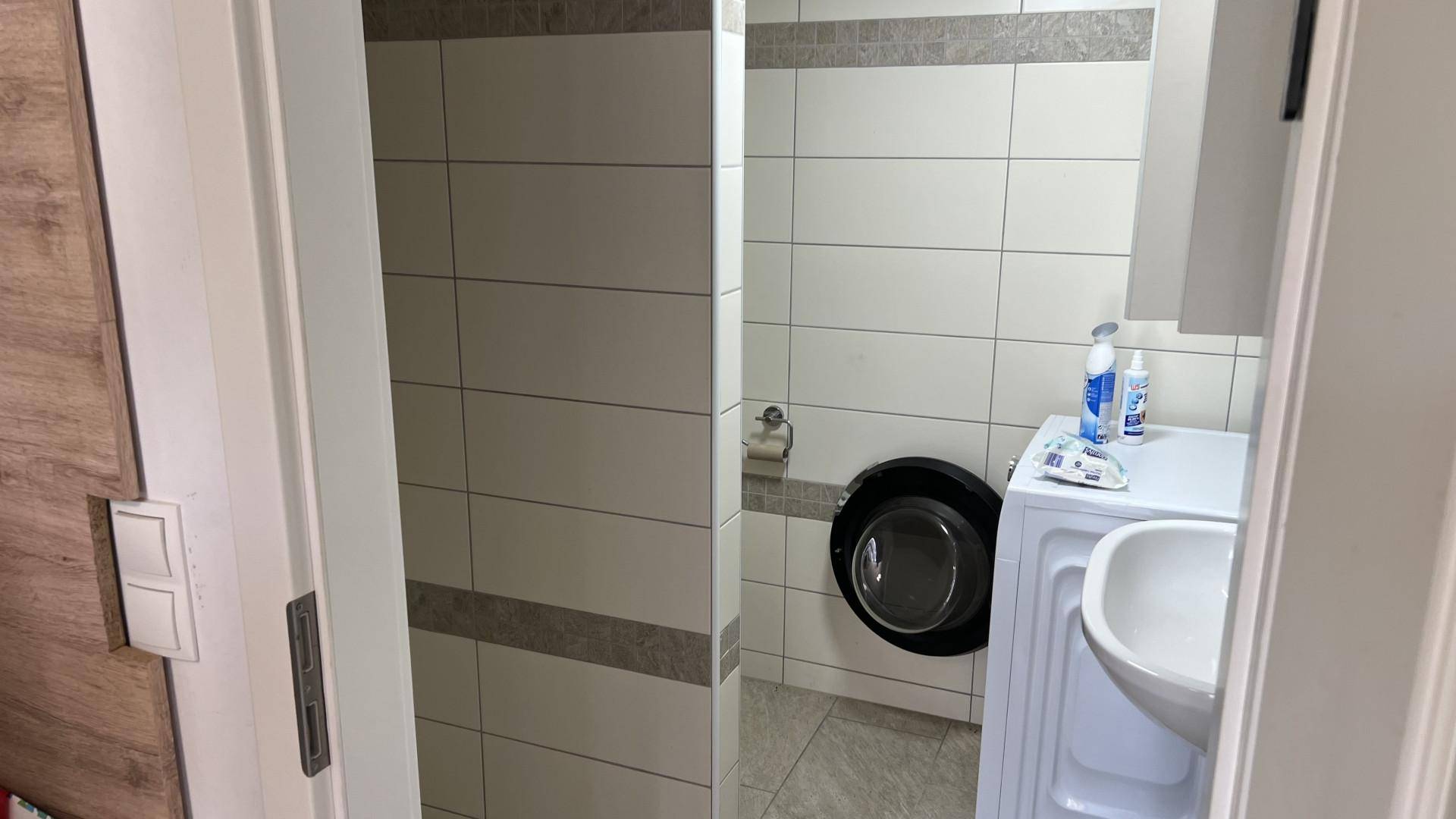 Kleines Badezimmer mit Waschmaschine, Waschbecken und Toilette, gefliest.