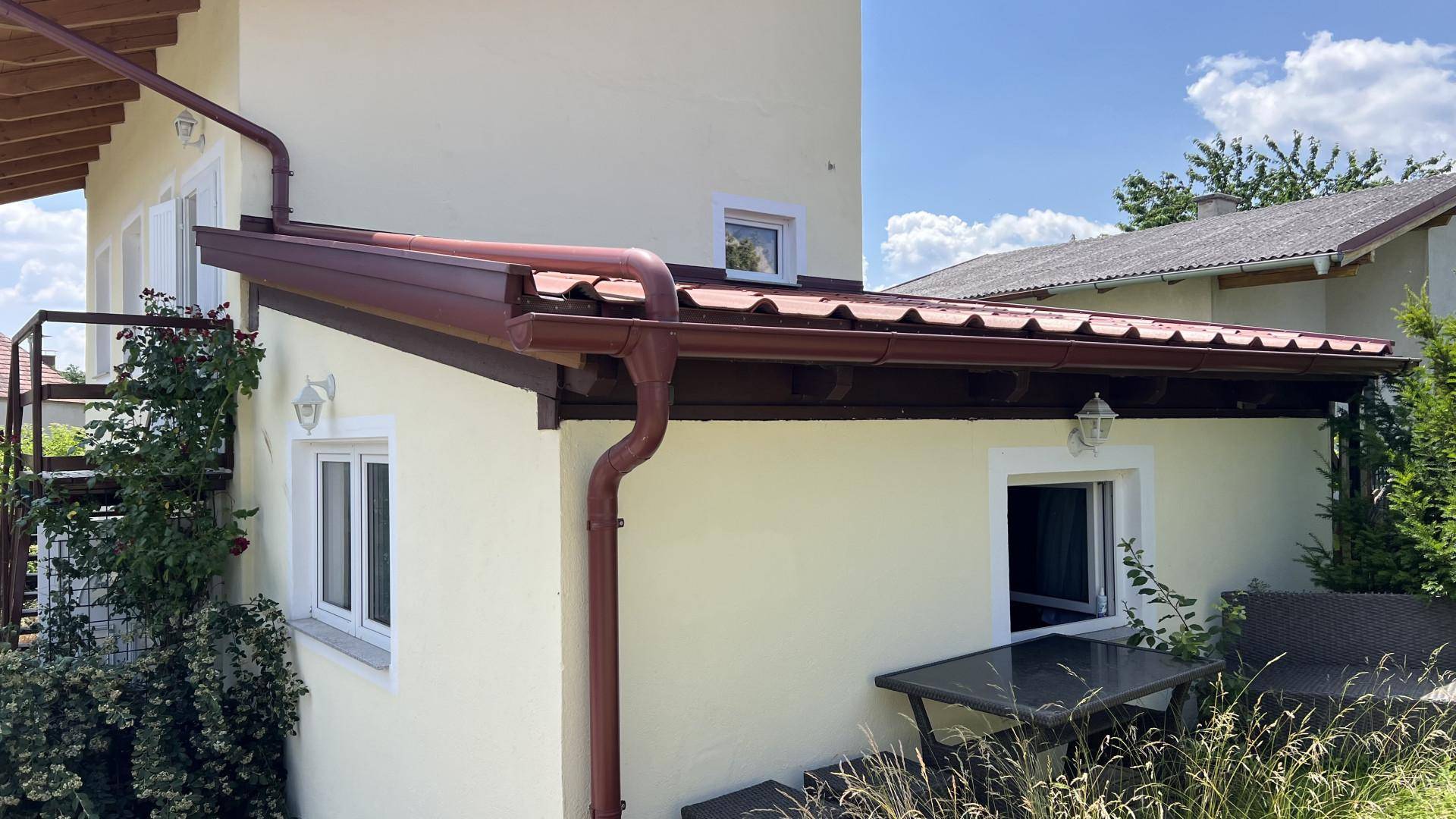 Seitenansicht des Hauses mit gelber Fassade, rotem Dach und einem kleinen Außentisch.