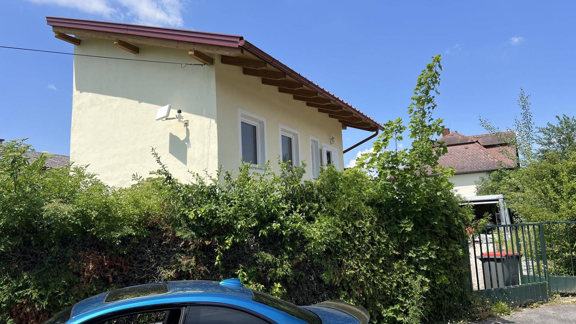 Seitenansicht des Hauses mit gelber Fassade und rotem Dach, umgeben von viel Grün.