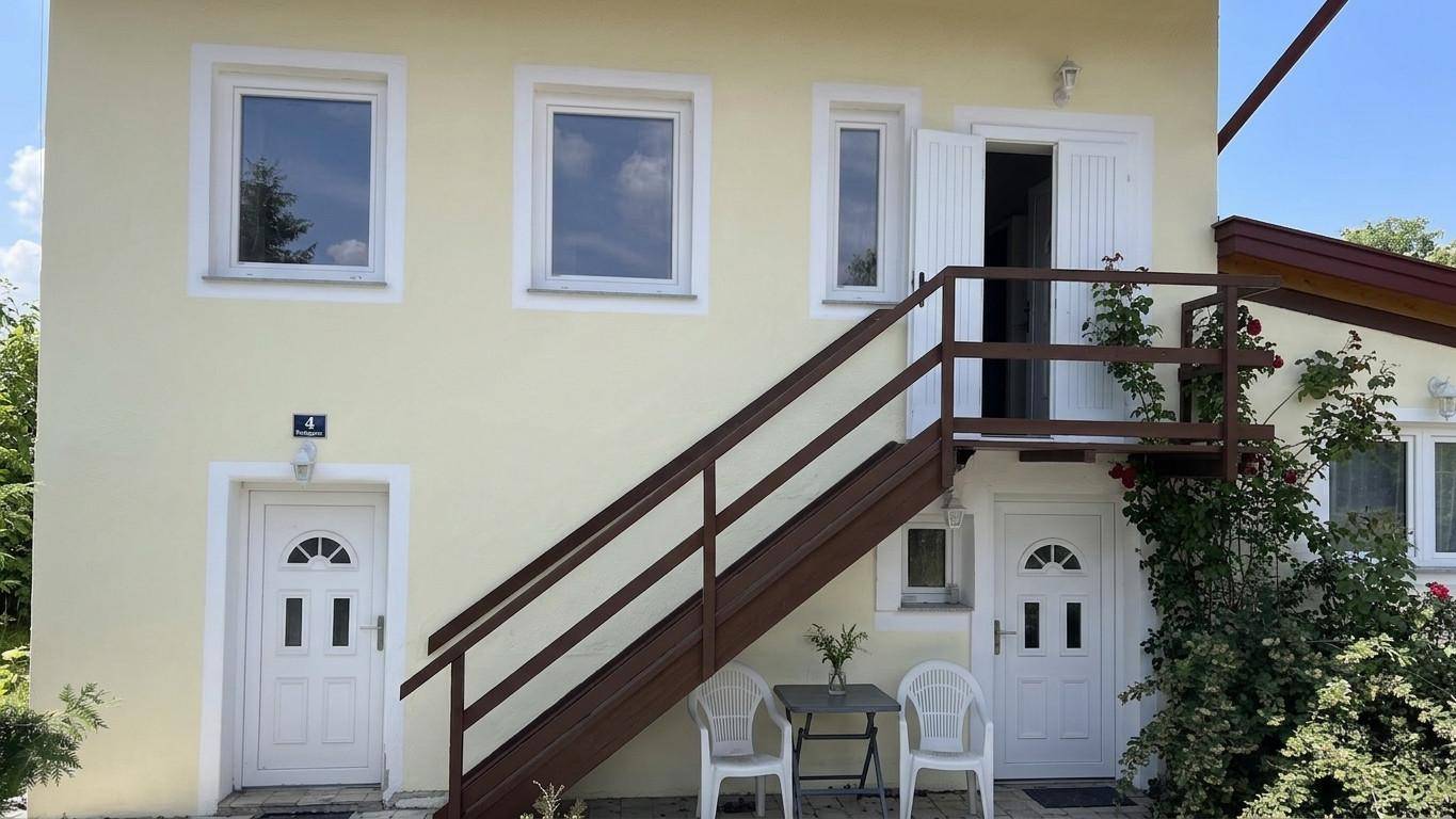 Vorderansicht des Hauses mit zwei Eingängen, Außentreppe und kleinem Sitzbereich.