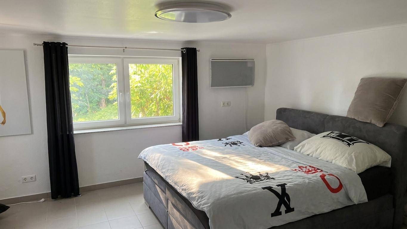Schlafzimmer mit Doppelbett, großem Fenster und Infrarotheizung an der Wand.