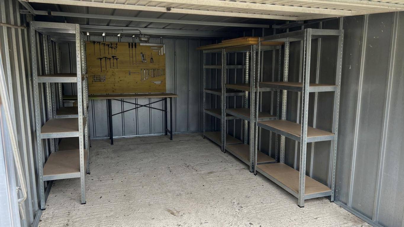 Innenansicht eines Metallschuppens oder einer Garage mit Regalen und Werkbank.