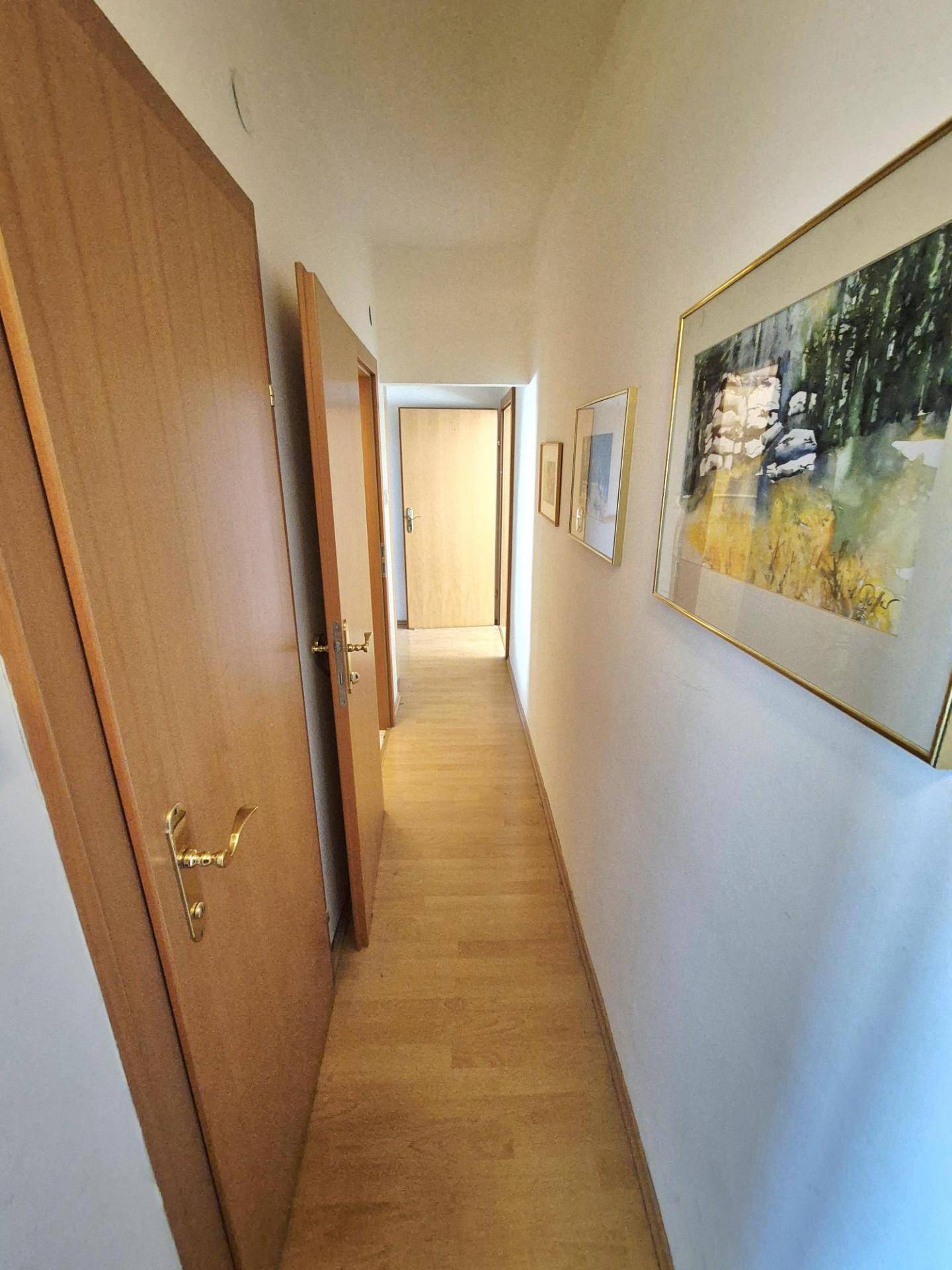 Heller Flur mit Holztüren, Parkettboden und gerahmten Bildern an der Wand.