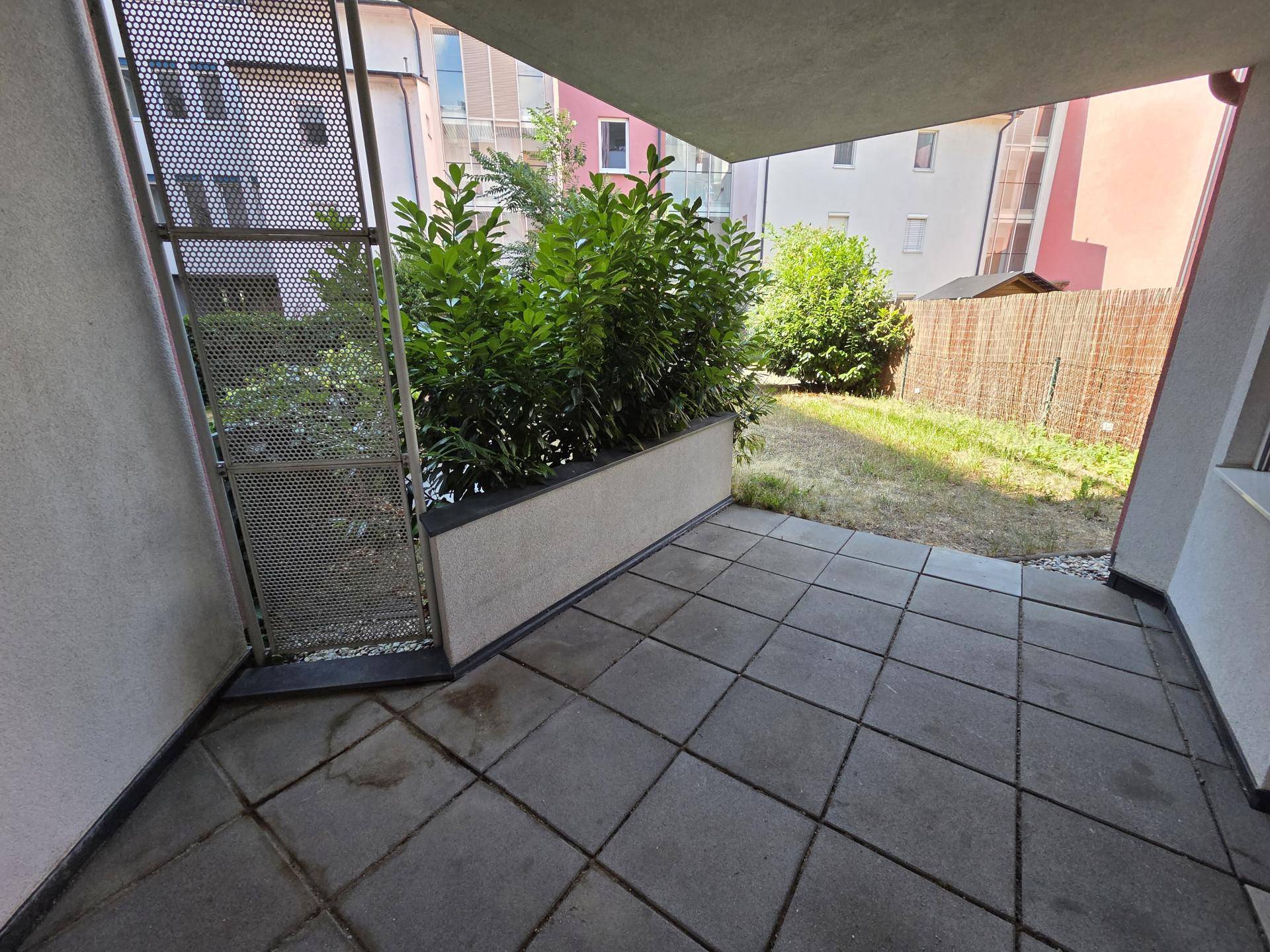 Überdachte Terrasse mit Steinplatten und Blick auf den Garten und umliegende Gebäude.
