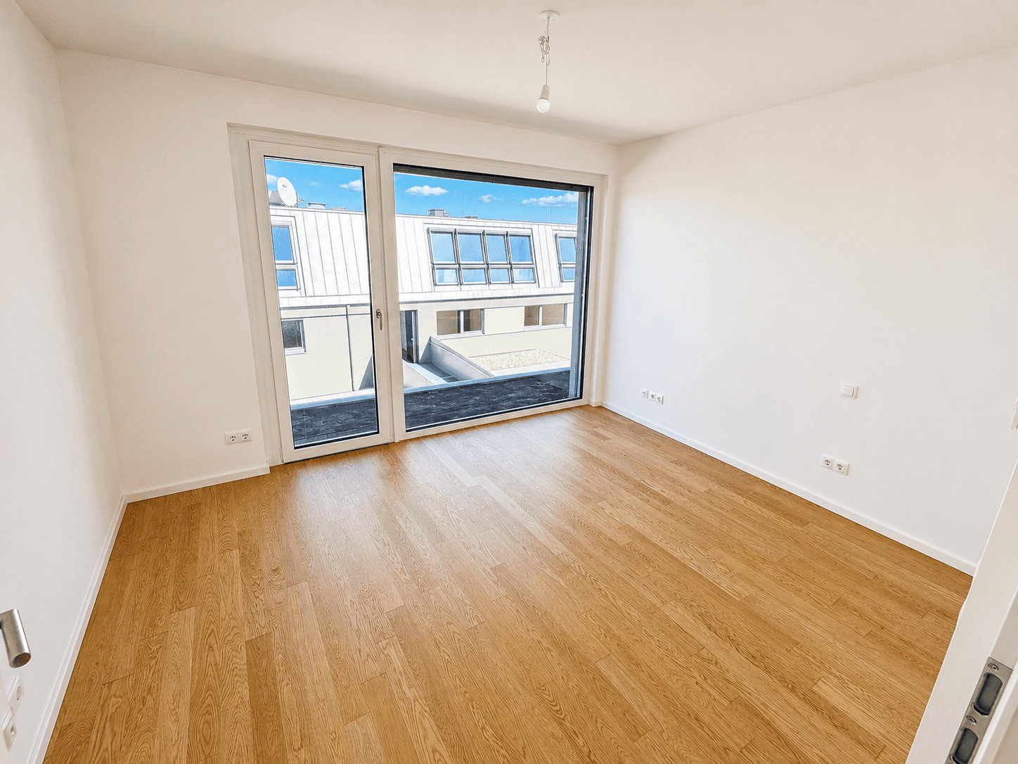 Helles Schlafzimmer mit Holzboden und großer Fensterfront, die einen Blick auf die umliegenden Dächer bietet.