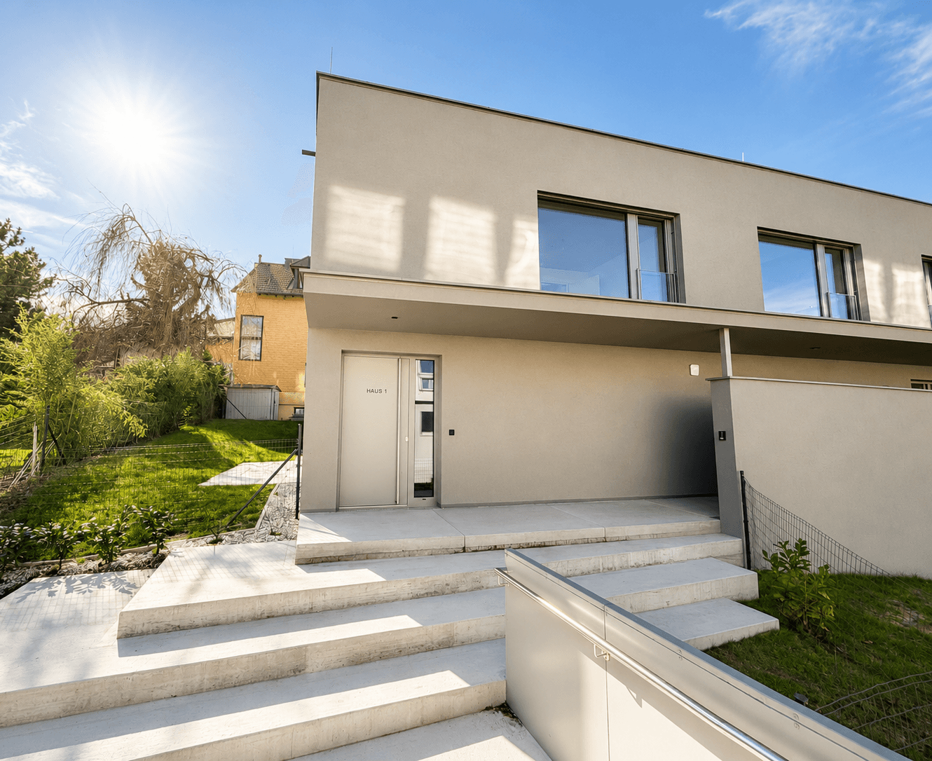 Moderne Architektur mit klarer Linienführung, heller Fassade und großzügigen Fensterflächen unter blauem Himmel.