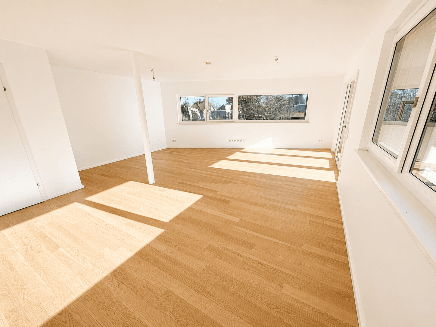 Lichtdurchfluteter Wohnraum mit Eichenparkett, vielen Fenstern und frischer, weißer Wandfarbe.
