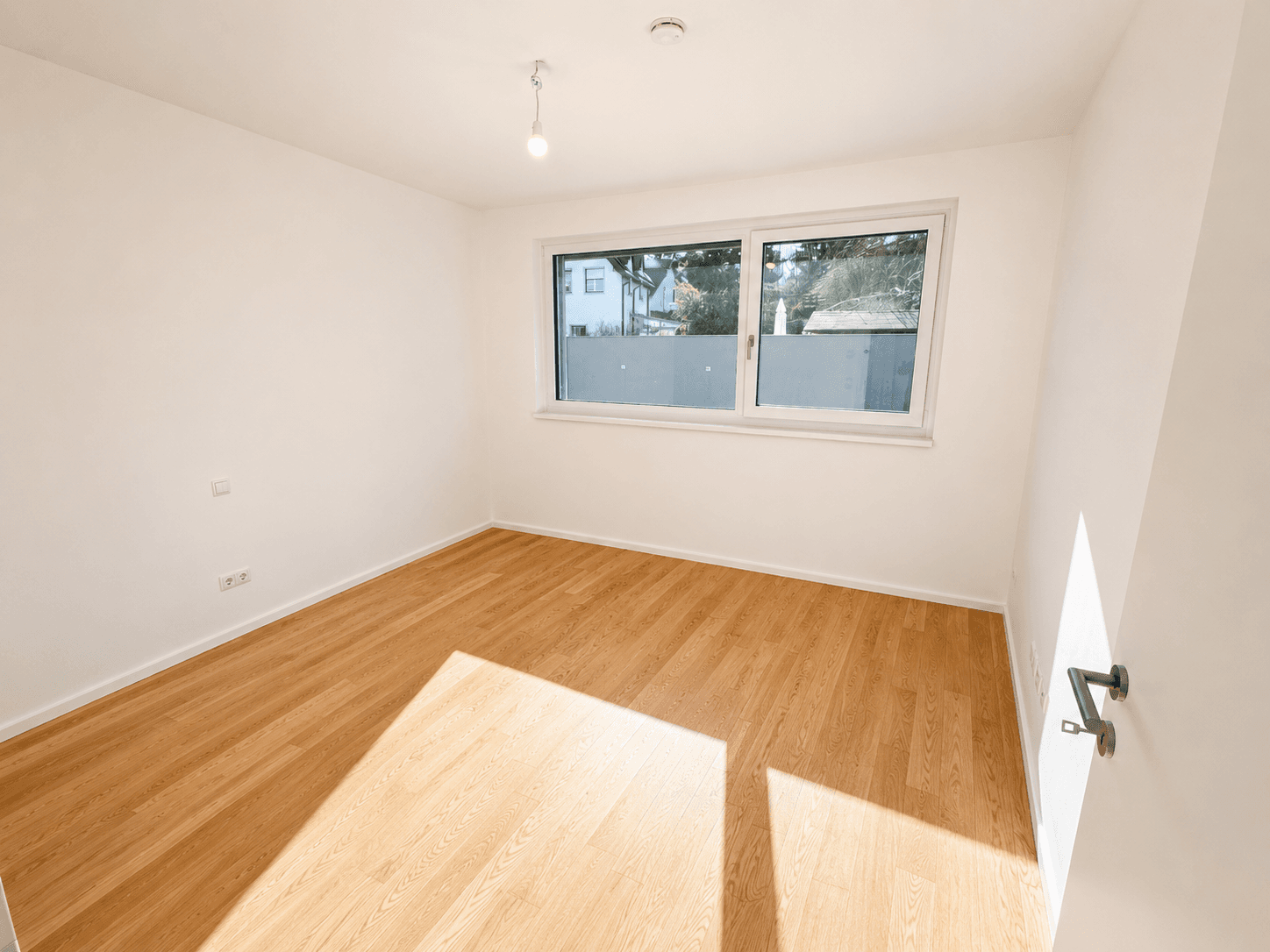 Sonnenverwöhntes Schlafzimmer mit Parkettboden, neutralen Wänden und Blick ins Grüne.