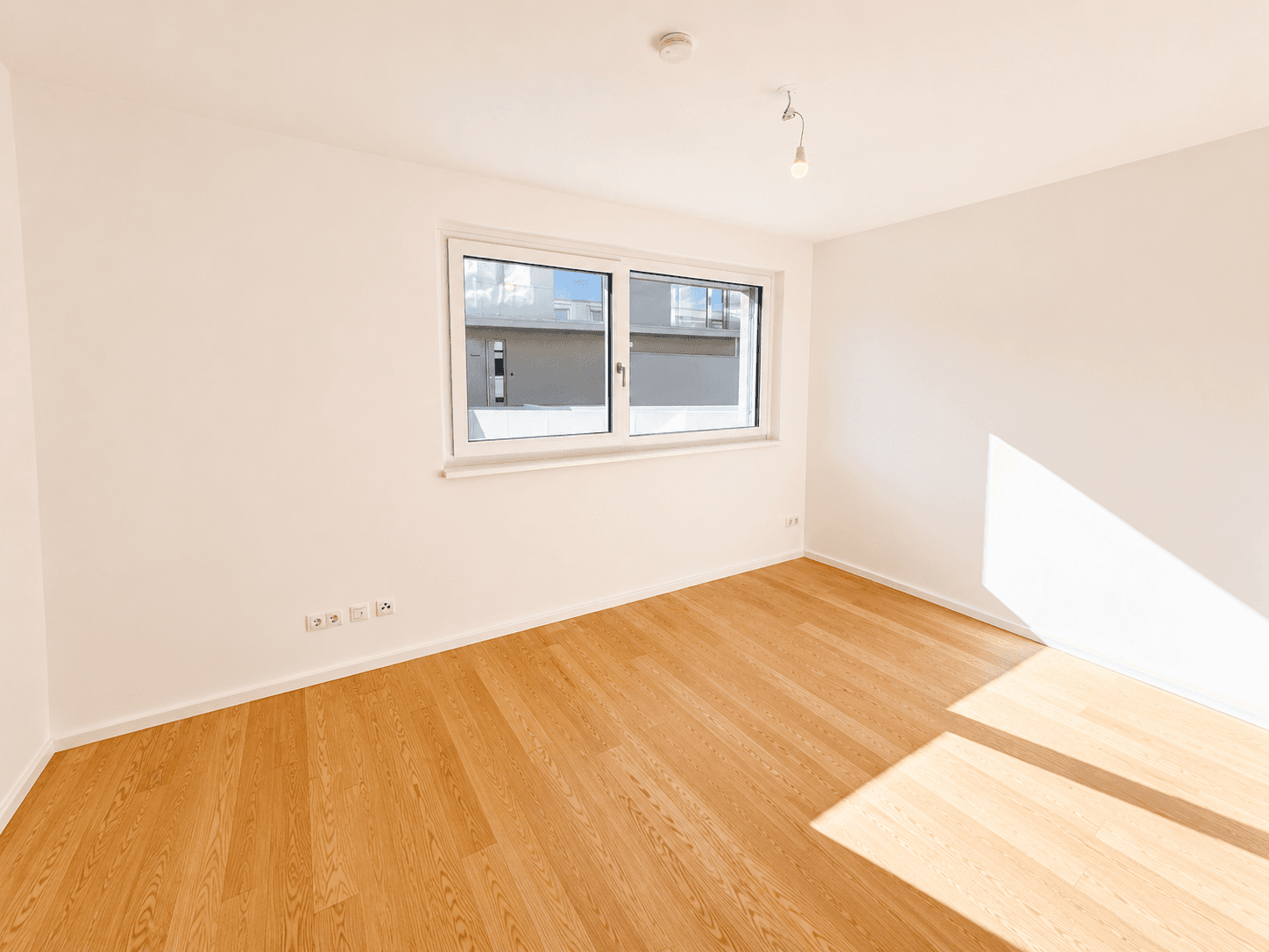 Helles Schlafzimmer mit Holzboden, weiß gestrichenen Wänden und einem großen Fenster.