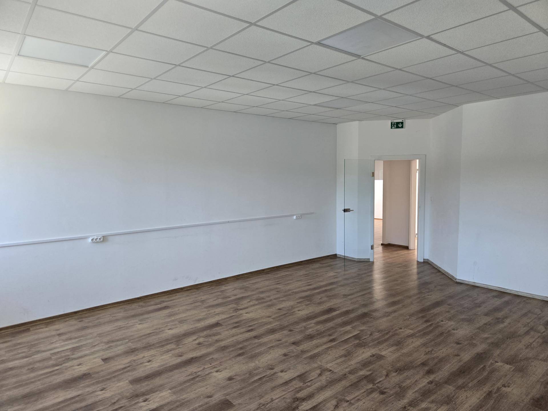 Heller Büroraum mit Laminatboden, abgehängter Decke und einer modernen Glastür.