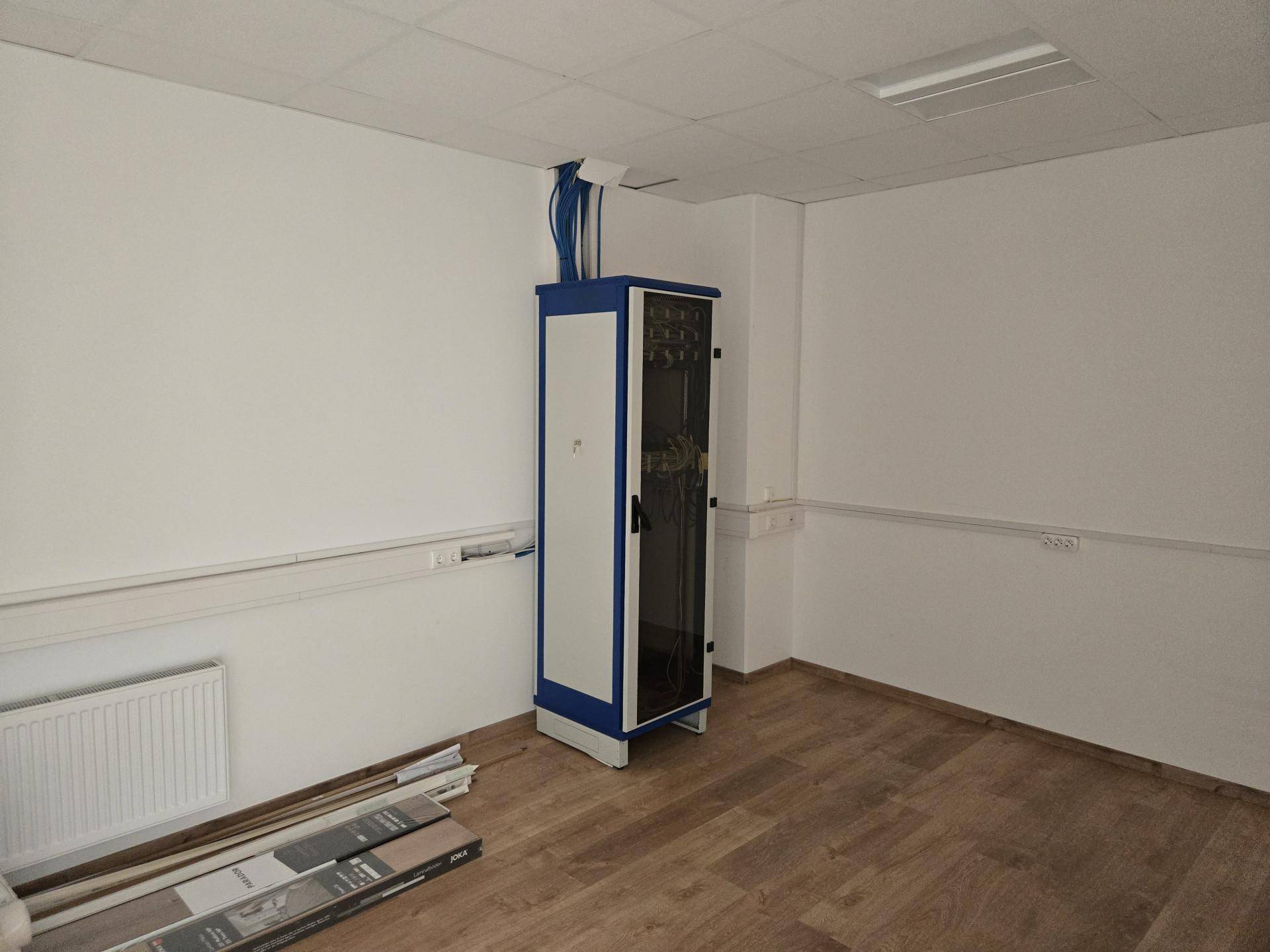 Kleiner Raum mit einem Serverschrank, Laminatboden und abgehängter Decke, ideal für IT-Infrastruktur.