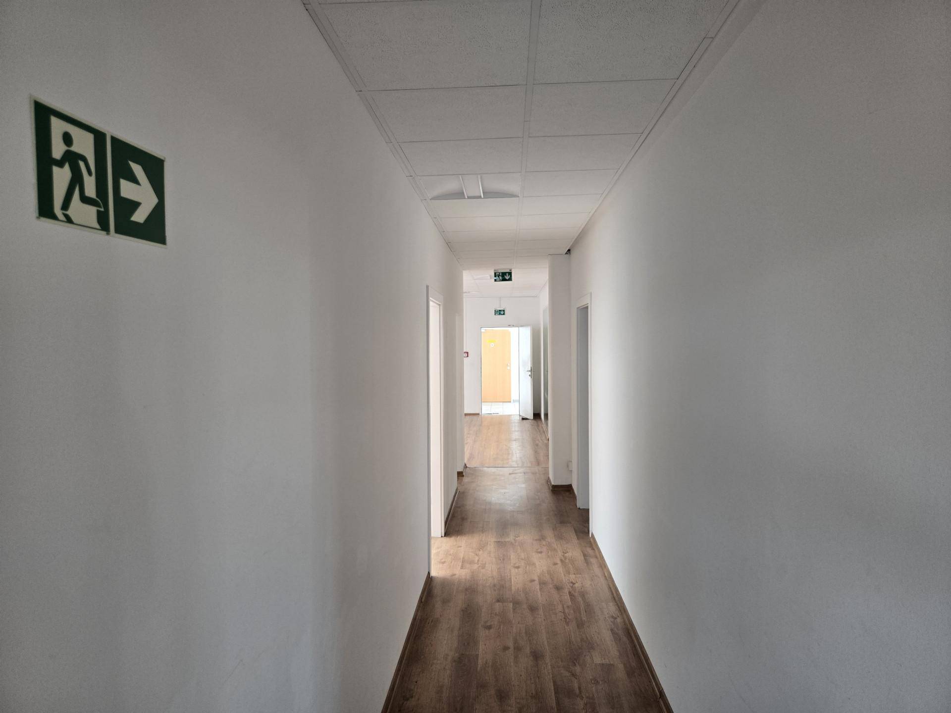 Langer, heller Flur mit Laminatboden und Notausgangsschildern, der zu weiteren Räumen führt.