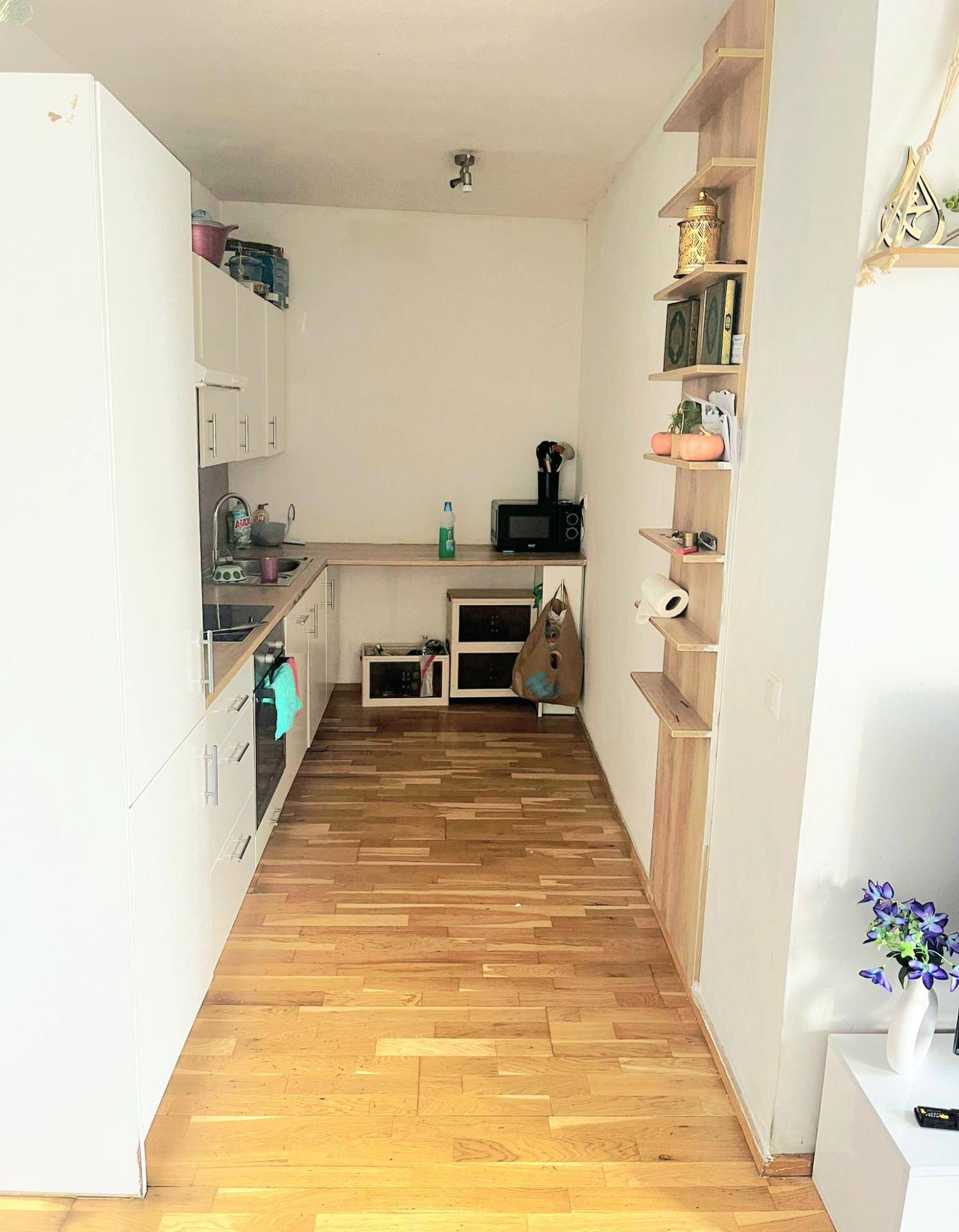 Helle, schmale Küche mit weißen Schränken, Holzregalen und Parkettboden.