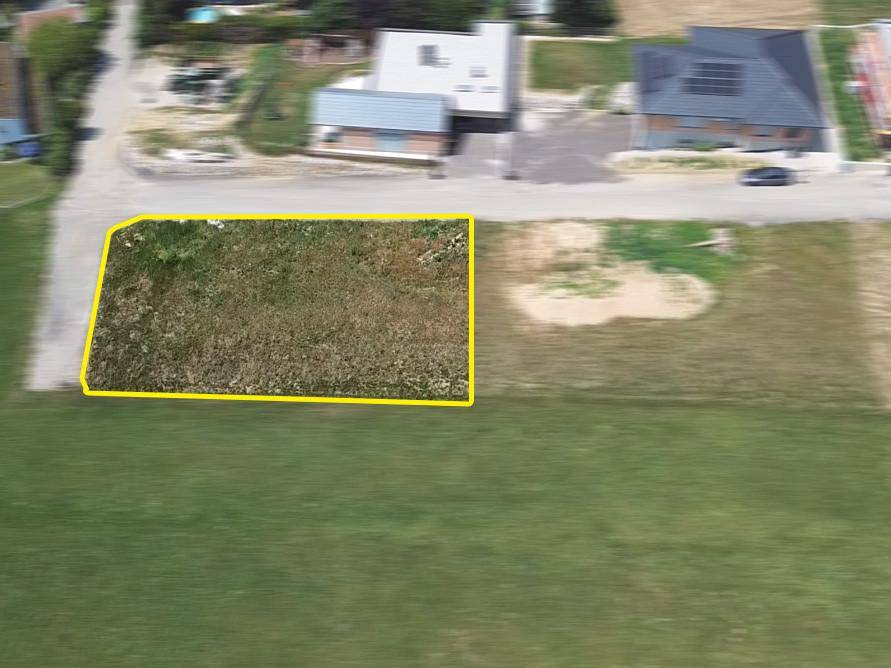 Luftaufnahme eines rechteckigen Baugrundstücks mit gelber Umrandung neben einer Straße.